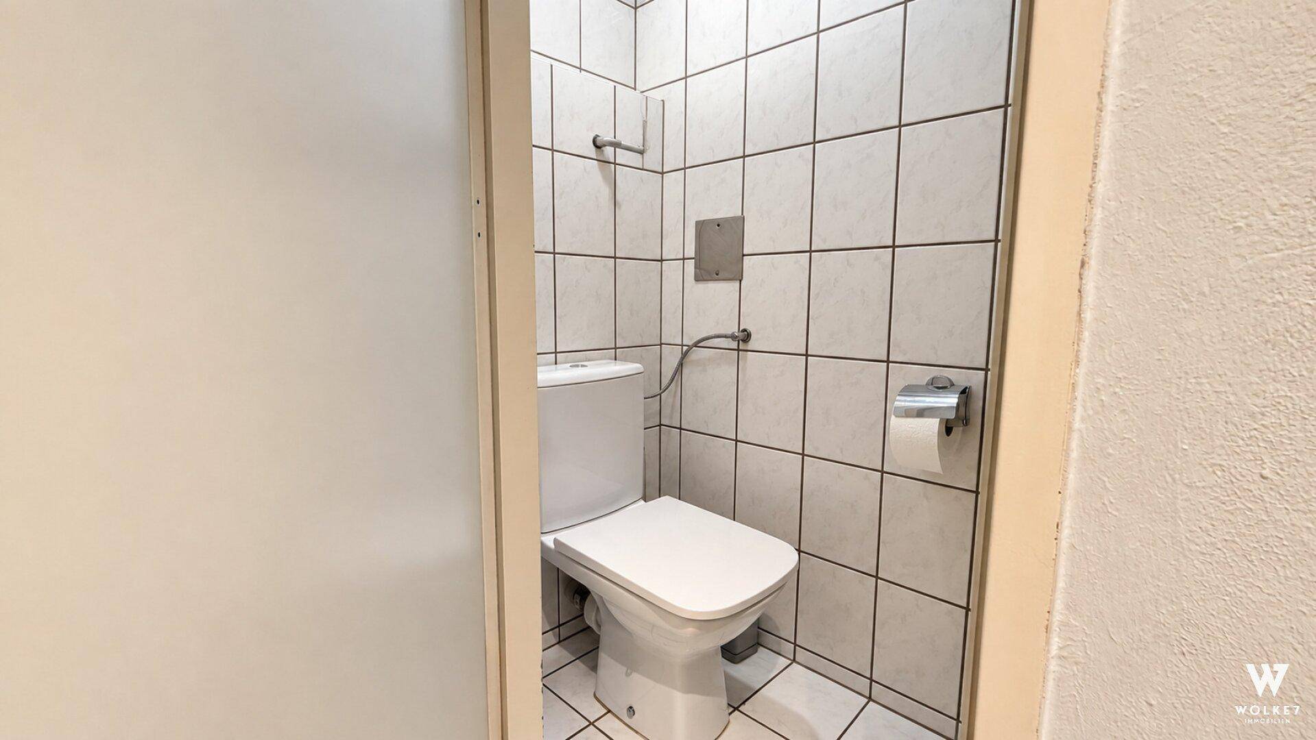 Kleines WC mit weißer Toilette und hellen Fliesen an den Wänden, praktisch und funktional gestaltet.
