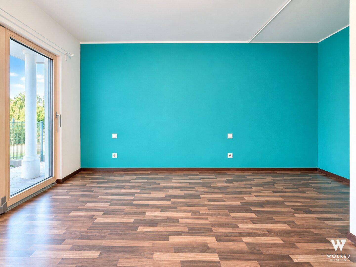 Großes Zimmer mit türkisfarbener Akzentwand und Laminatboden, mit Zugang nach draußen.