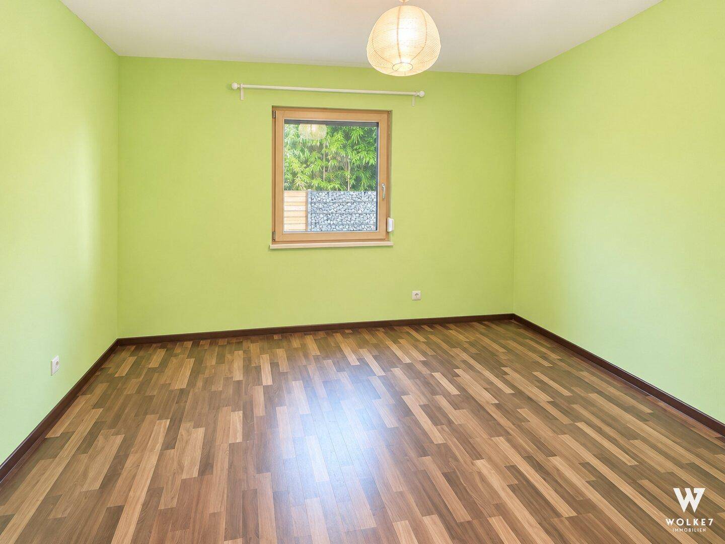 Helles Zimmer mit grünen Wänden und Laminatboden, geeignet als Kinder- oder Gästezimmer.
