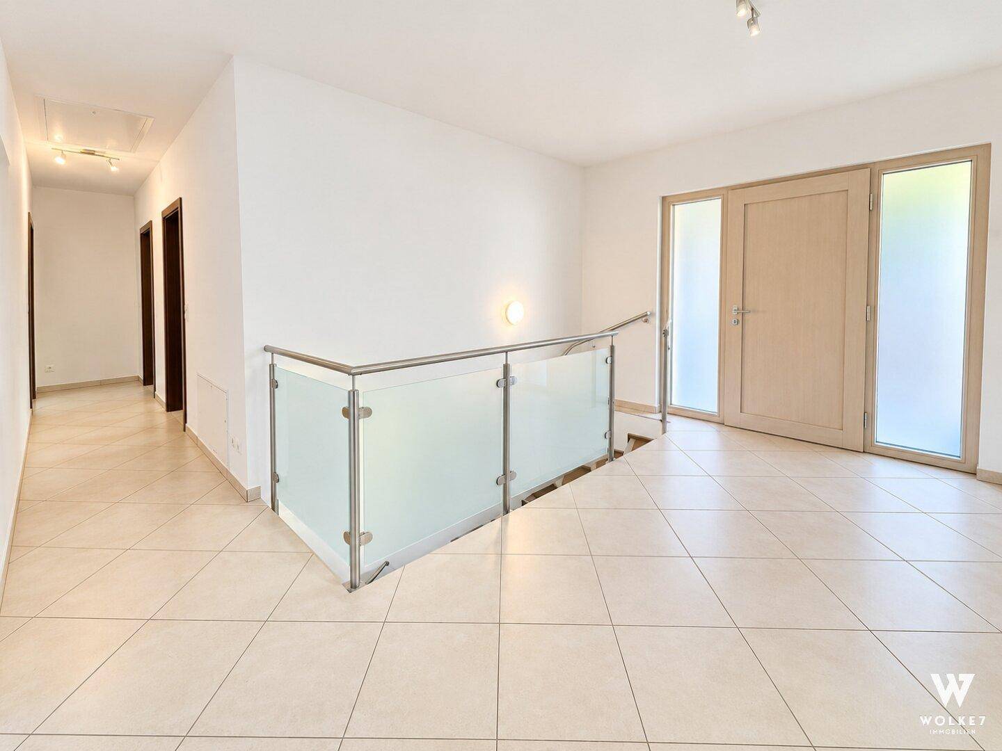Heller Flur mit Fliesenboden und moderner Glasbrüstung zur Treppe.