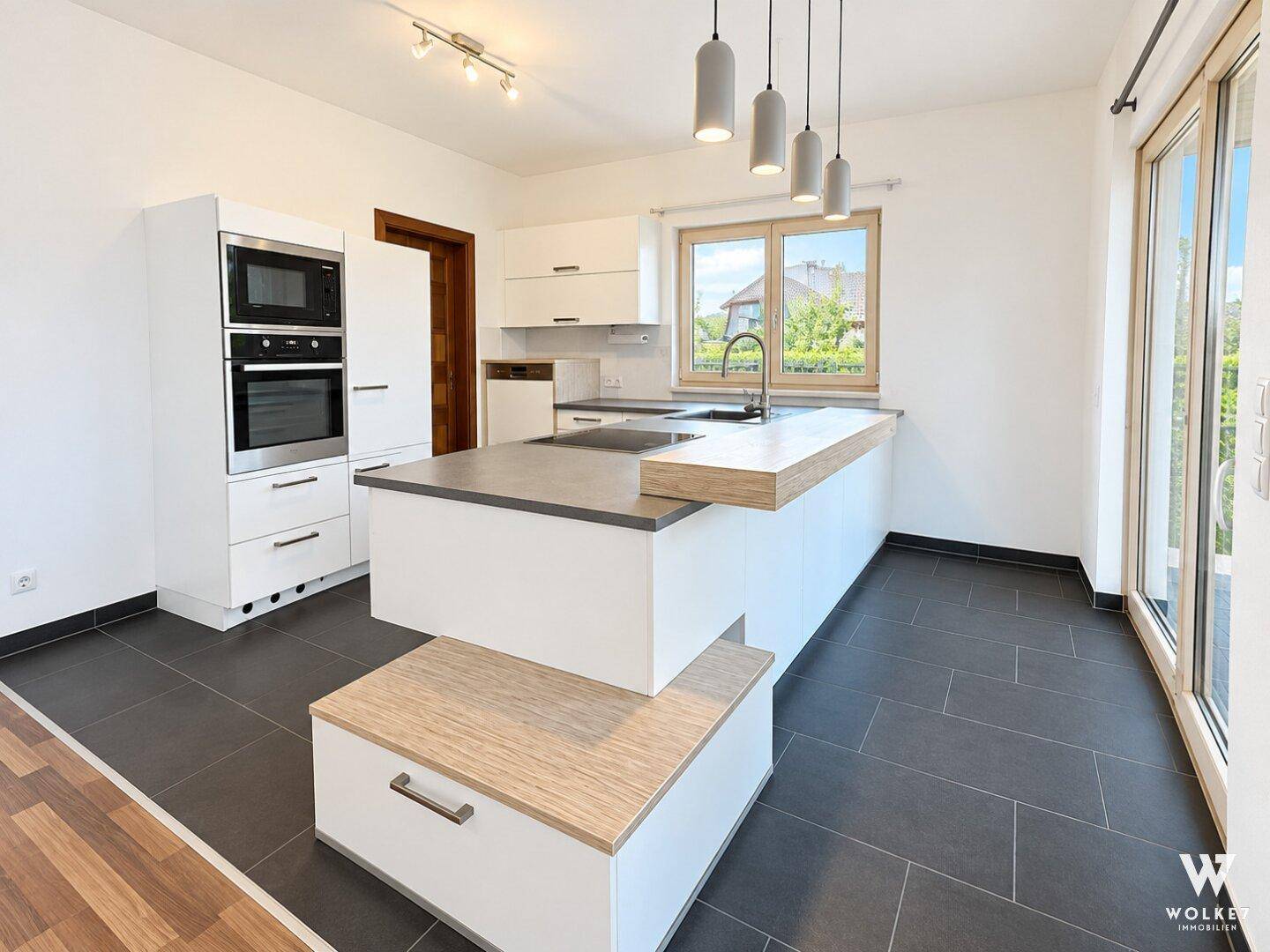Moderne Einbauküche mit Kochinsel, integrierten Geräten und dunklem Fliesenboden.