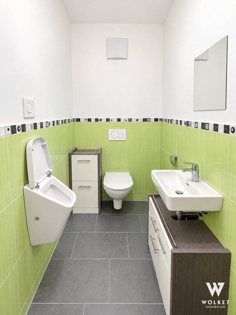 Modernes Gäste-WC mit Wand-WC, Bidet und grün gefliesten Wänden.