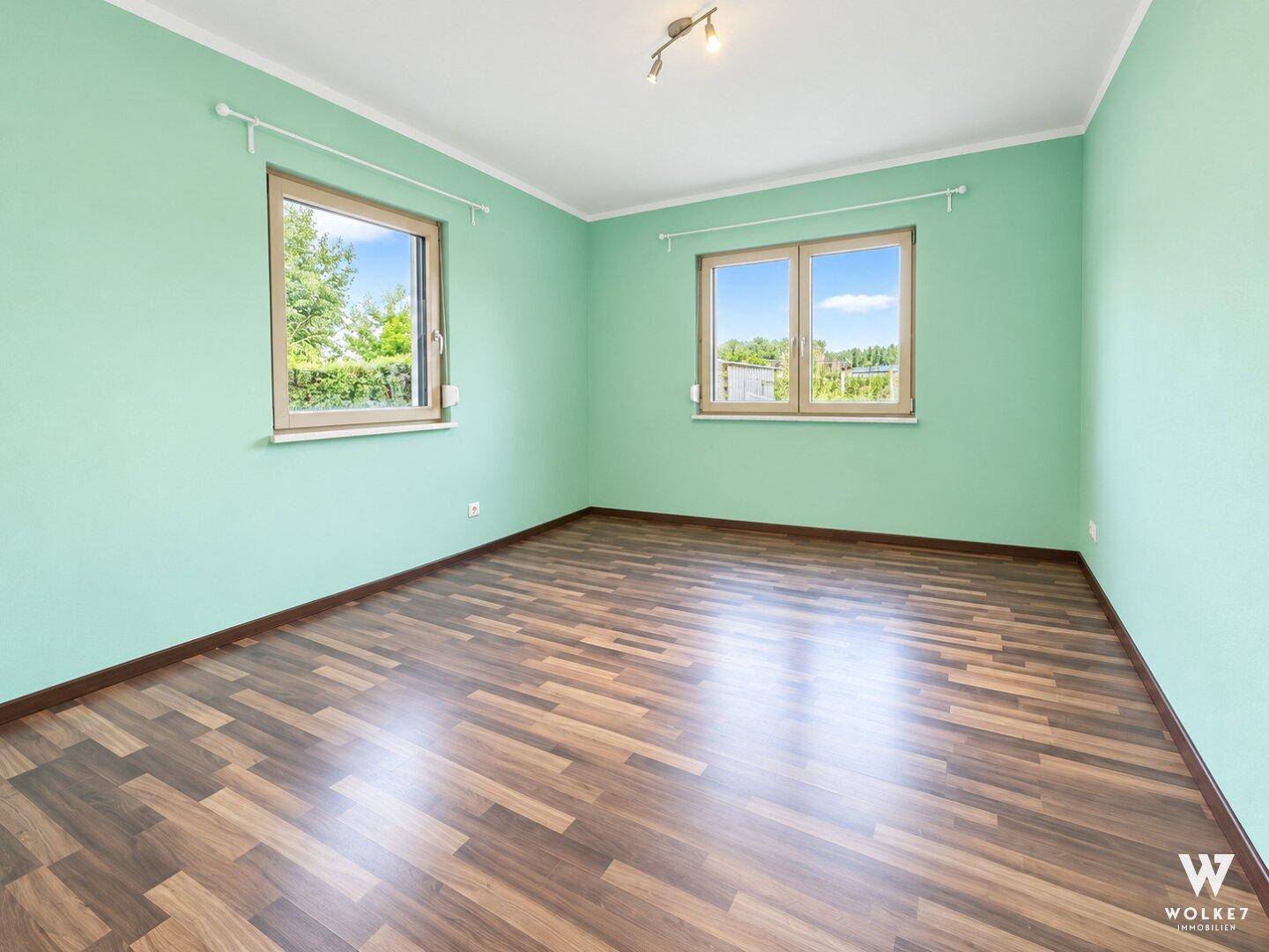 Geräumiges Zimmer mit hellgrünen Wänden und Laminatboden, ideal als Schlafzimmer.