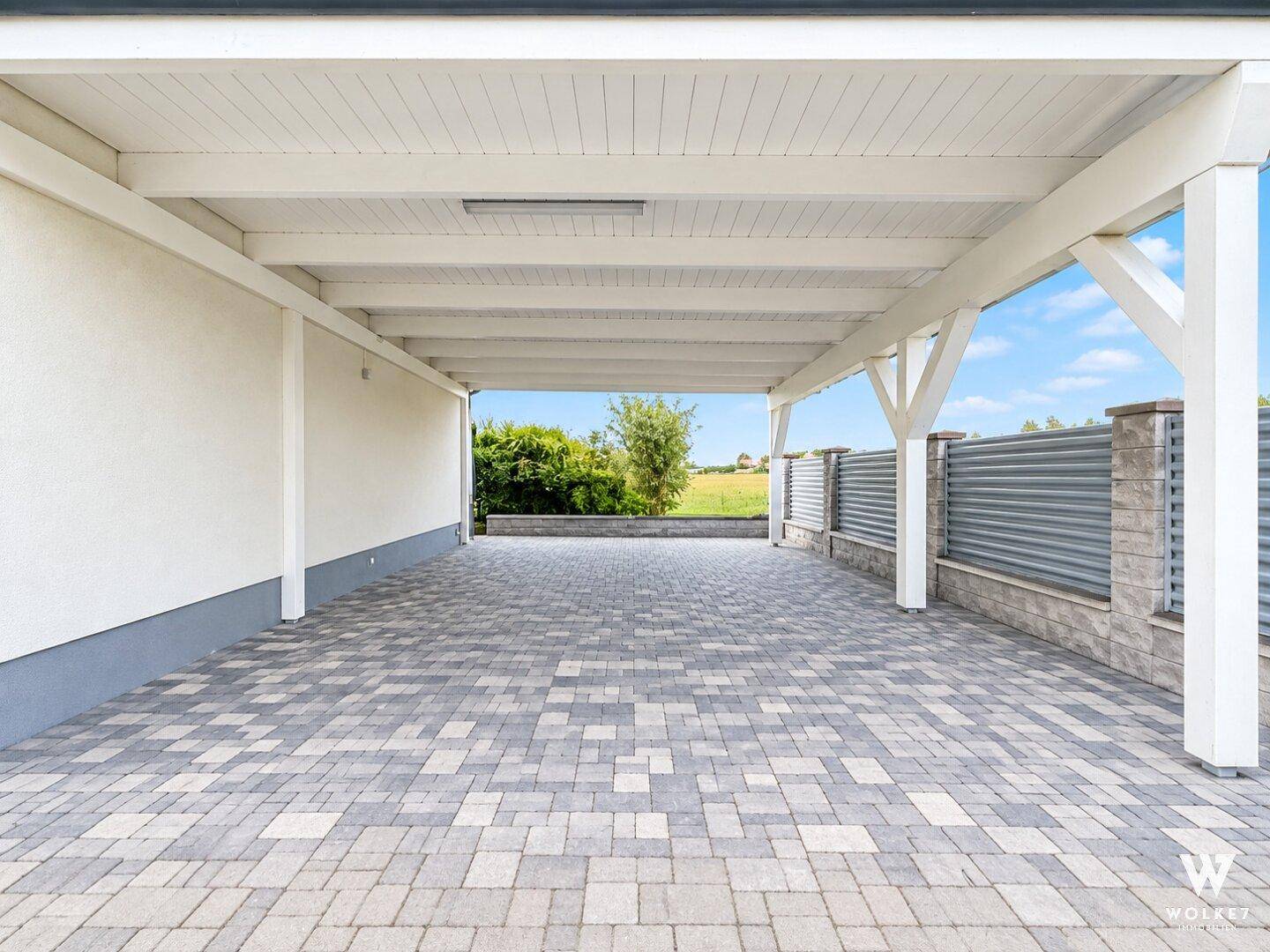 Geräumiger Carport mit gepflastertem Boden und Blick ins Grüne.