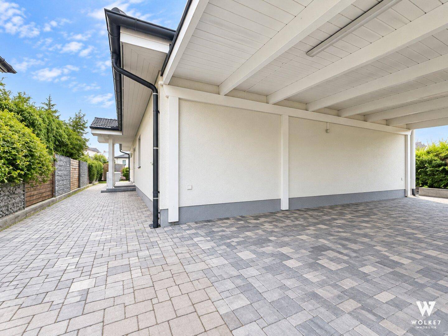 Seitenansicht des Hauses mit Carport und gepflasterter Zufahrt.