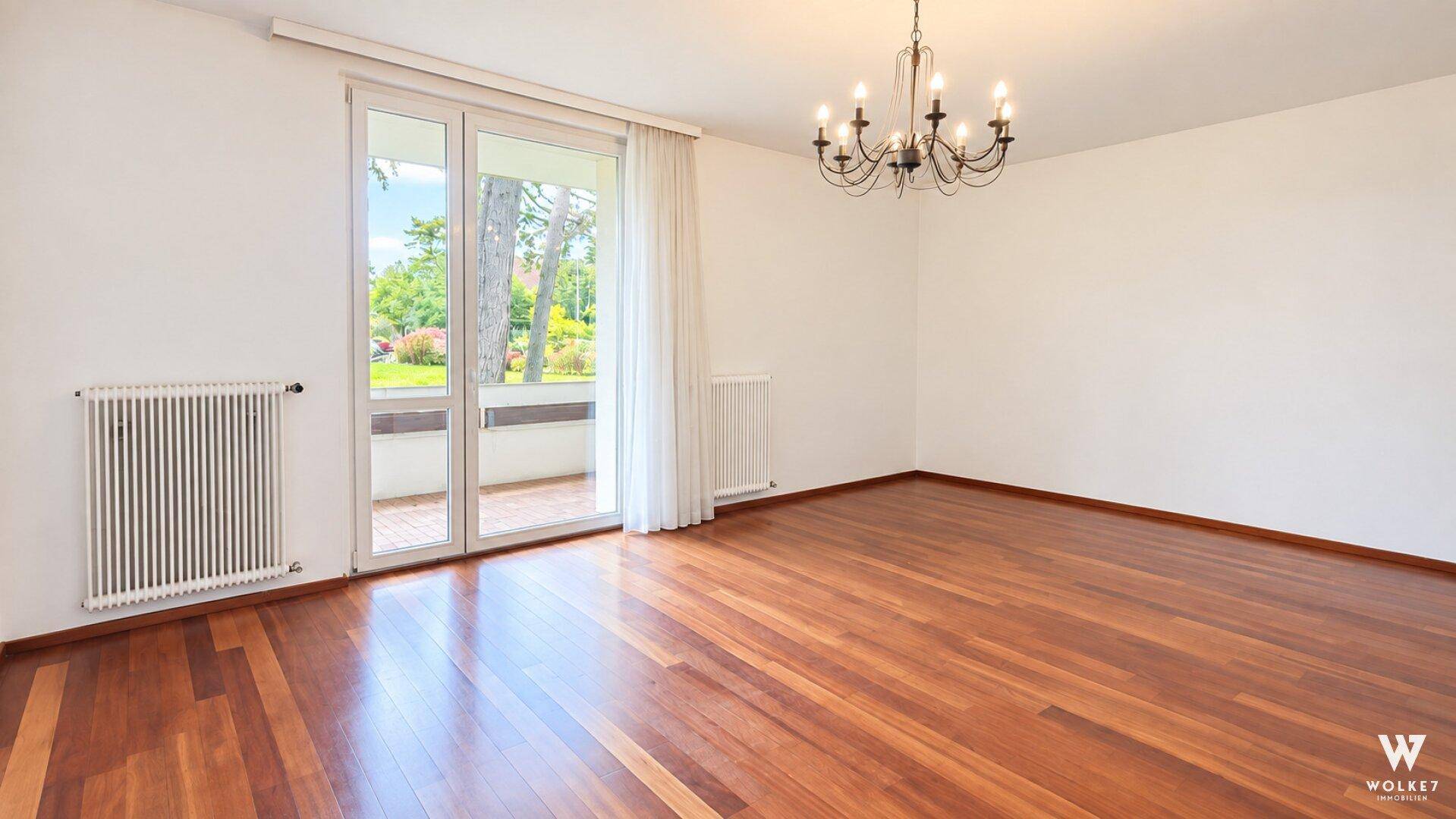 Helles, unmöbliertes Wohnzimmer mit glänzendem Holzboden und Zugang zu einem Außenbereich.
