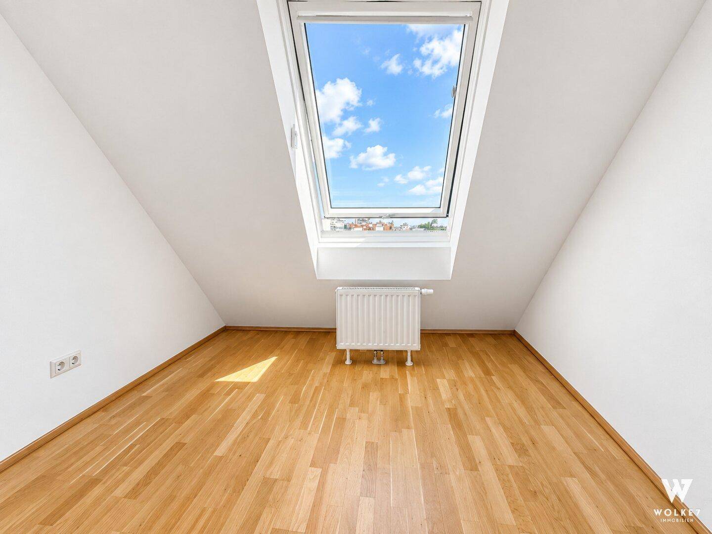 Helles Dachzimmer mit einem großen Dachfenster, schrägen Wänden und einem warmen Holzfußboden.