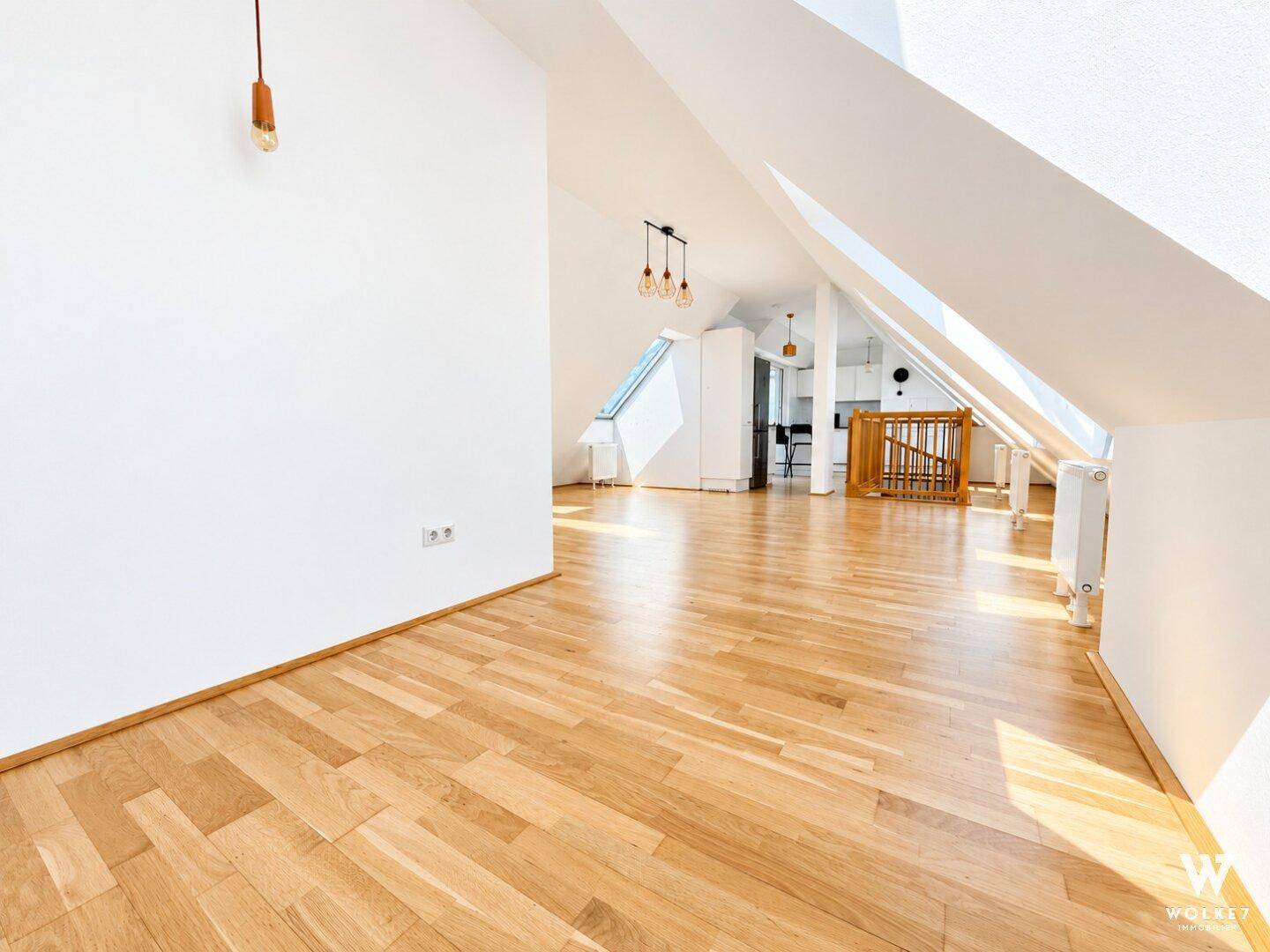 Offener Wohnbereich im Dachgeschoss mit Holzfußboden, schrägen Wänden und Blick zur modernen Küche.