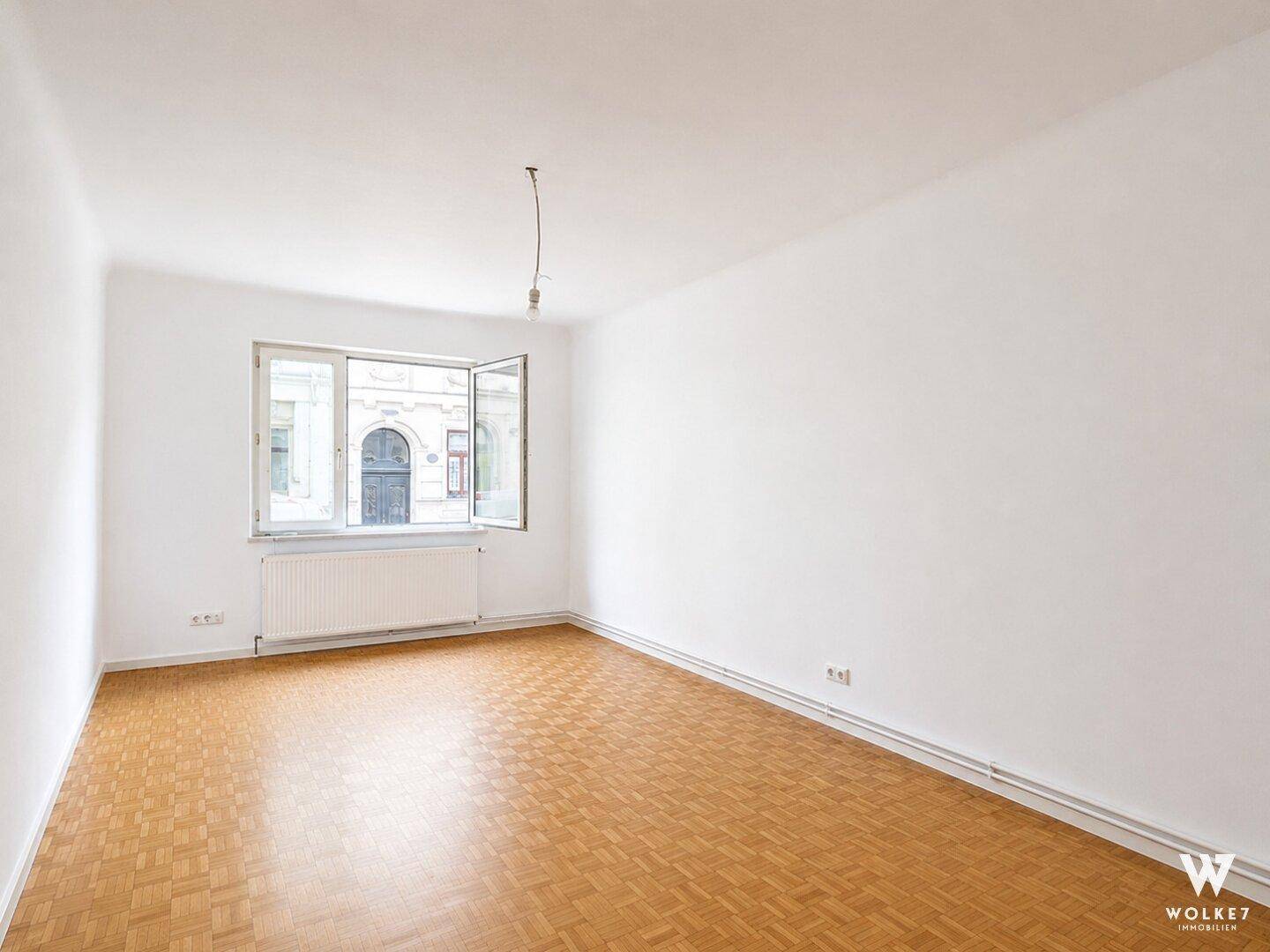 Helles, leeres Zimmer mit Parkettboden und großen Fenstern, ideal für individuelle Einrichtung.