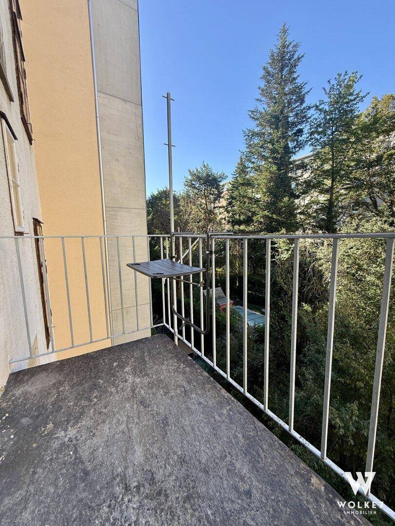 Kleiner Balkon mit Klapptisch und Blick ins Grüne sowie auf umliegende Gebäude.
