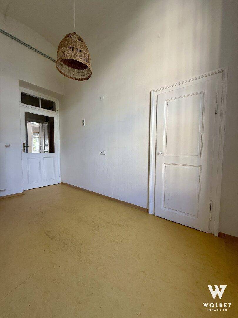 Heller Raum mit gelbem Boden, einer dekorativen Hängelampe und einer weißen Tür.