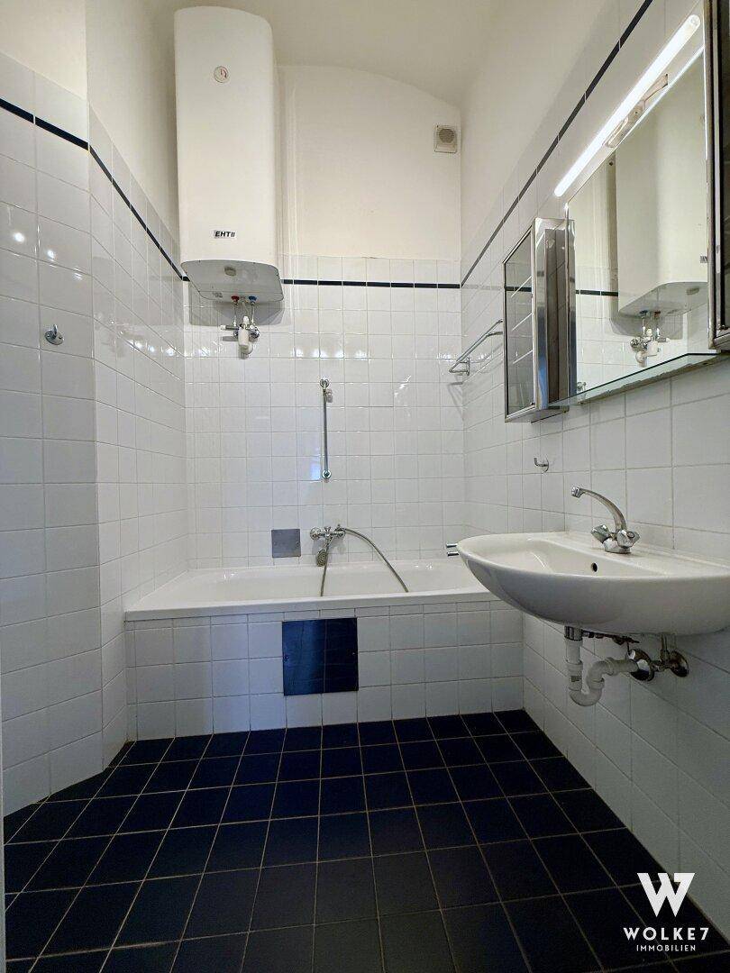 Badezimmer mit Badewanne, Waschbecken, Spiegelschrank und Warmwasserboiler.