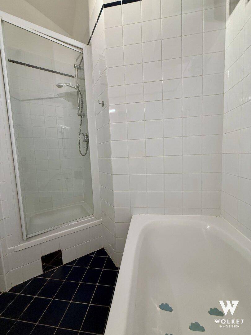 Badezimmer mit Badewanne und separater Duschkabine, gefliest in Weiß und Dunkelblau.