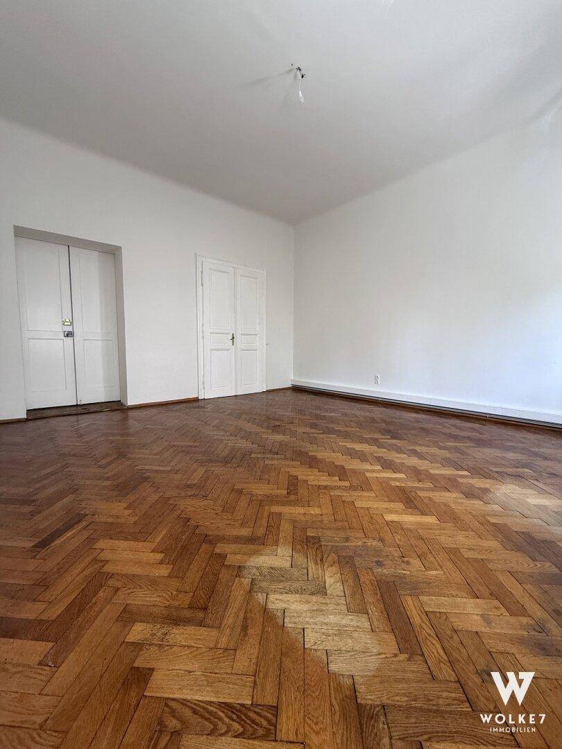 Geräumiges Zimmer mit elegantem Fischgrätparkett und hohen weißen Türen.