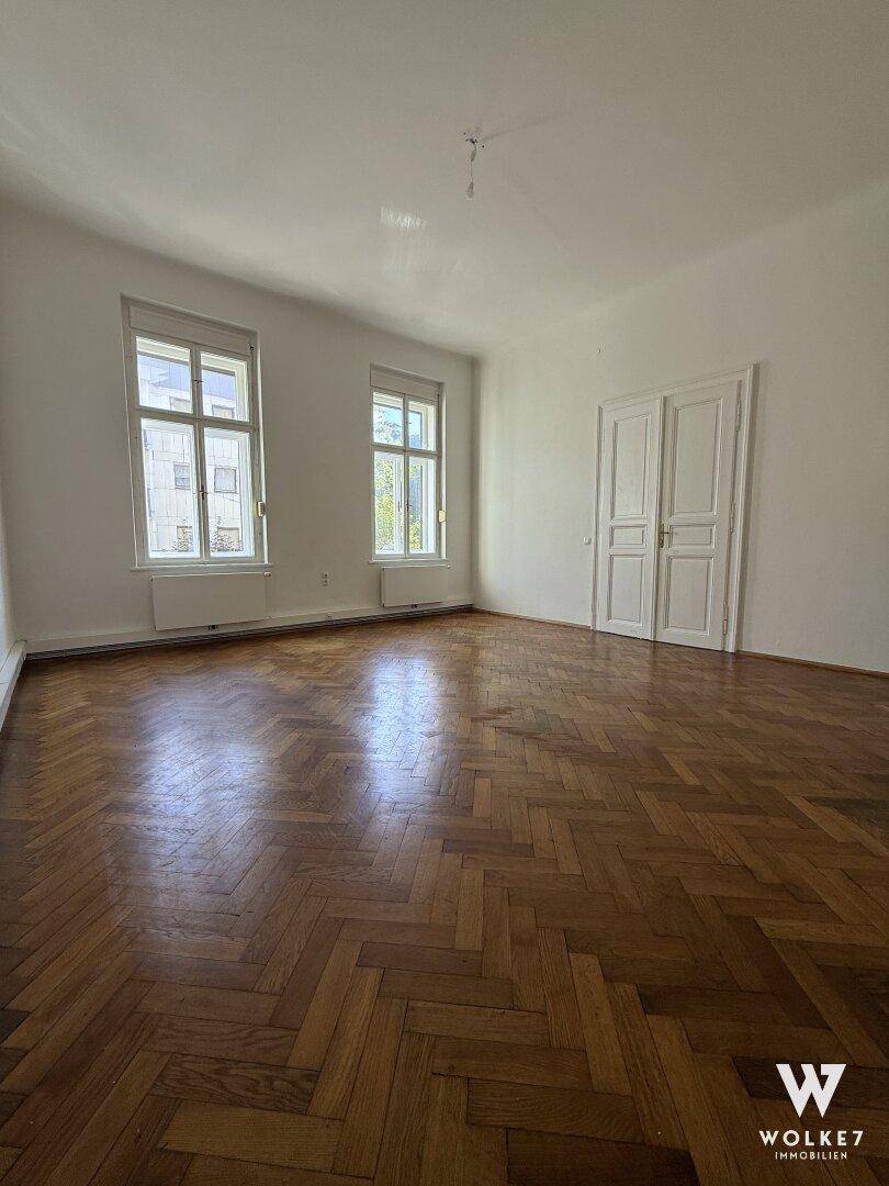 Helles Zimmer mit klassischem Fischgrätparkett und zwei Fenstern, die viel Licht hereinlassen.
