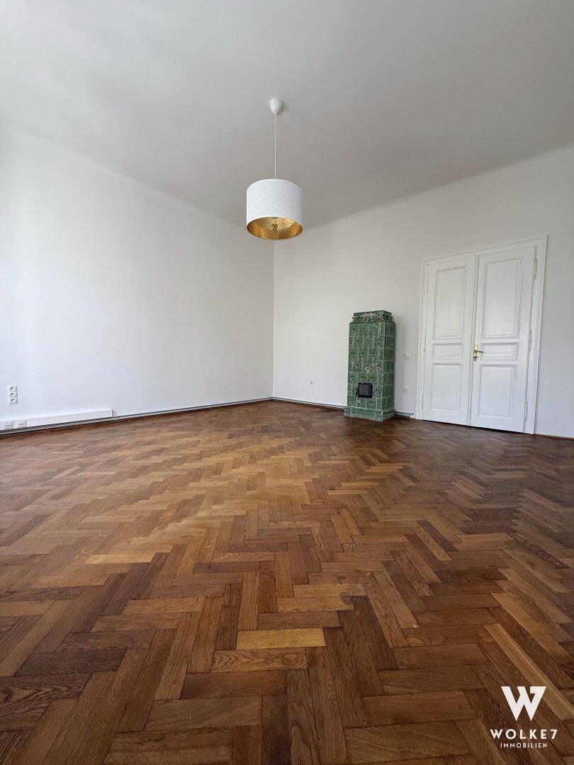 Geräumiges Zimmer mit Fischgrätparkett und einem dekorativen grünen Kachelofen.