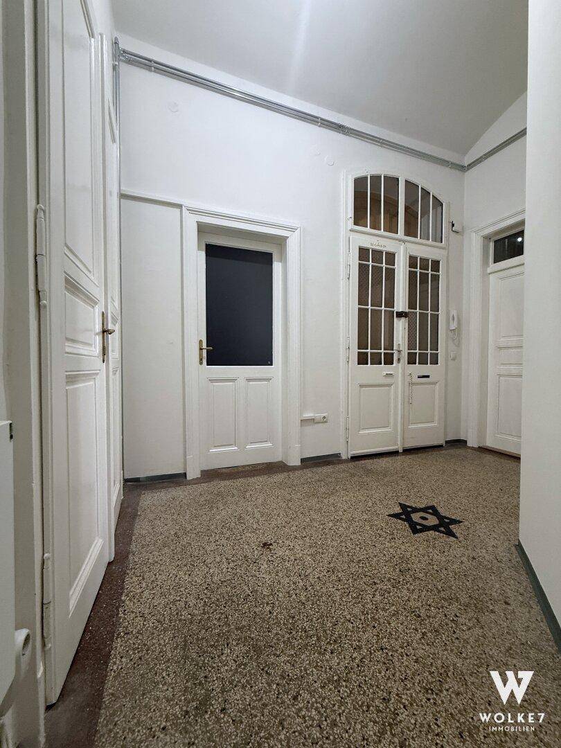 Eingangsbereich mit Terrazzoboden, dekorativem Sternmotiv und hohen weißen Türen.