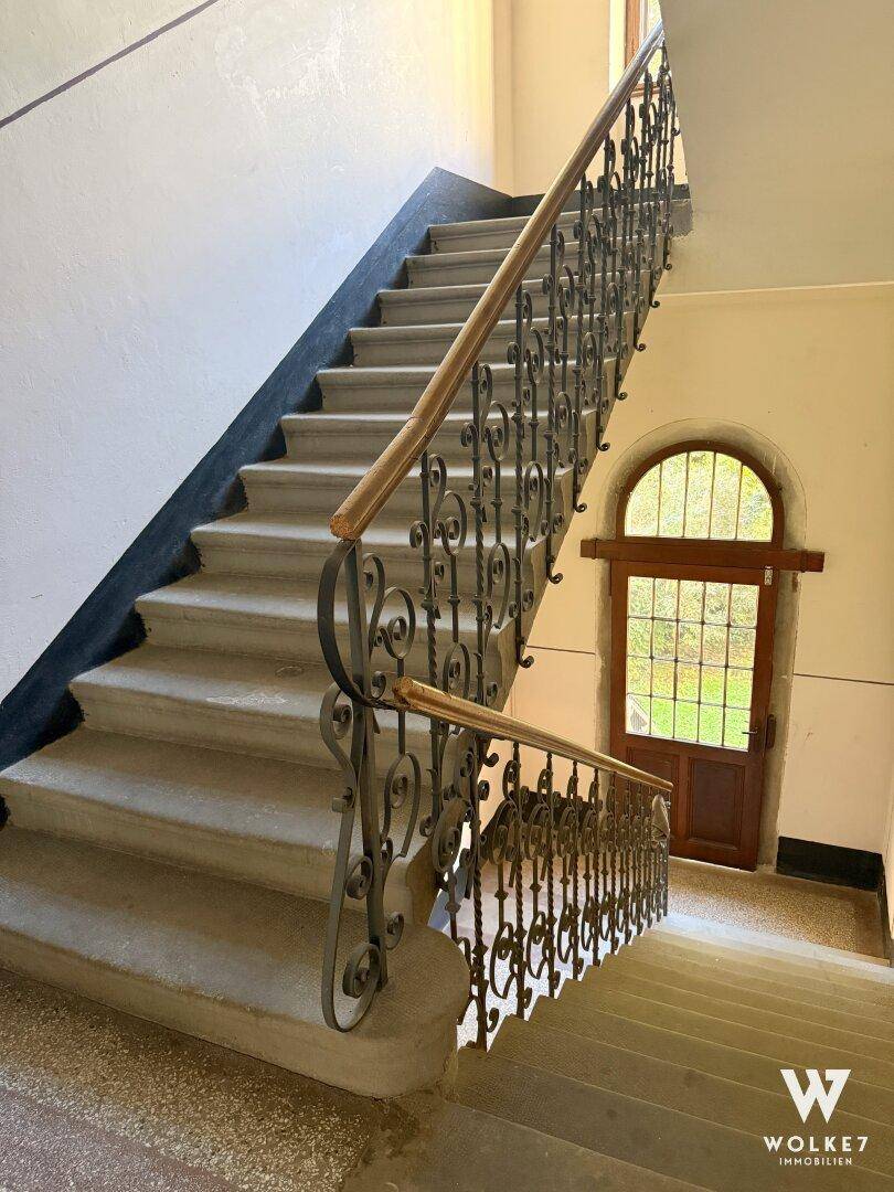 Elegantes Treppenhaus mit schmiedeeisernem Geländer und einem großen Rundbogenfenster.