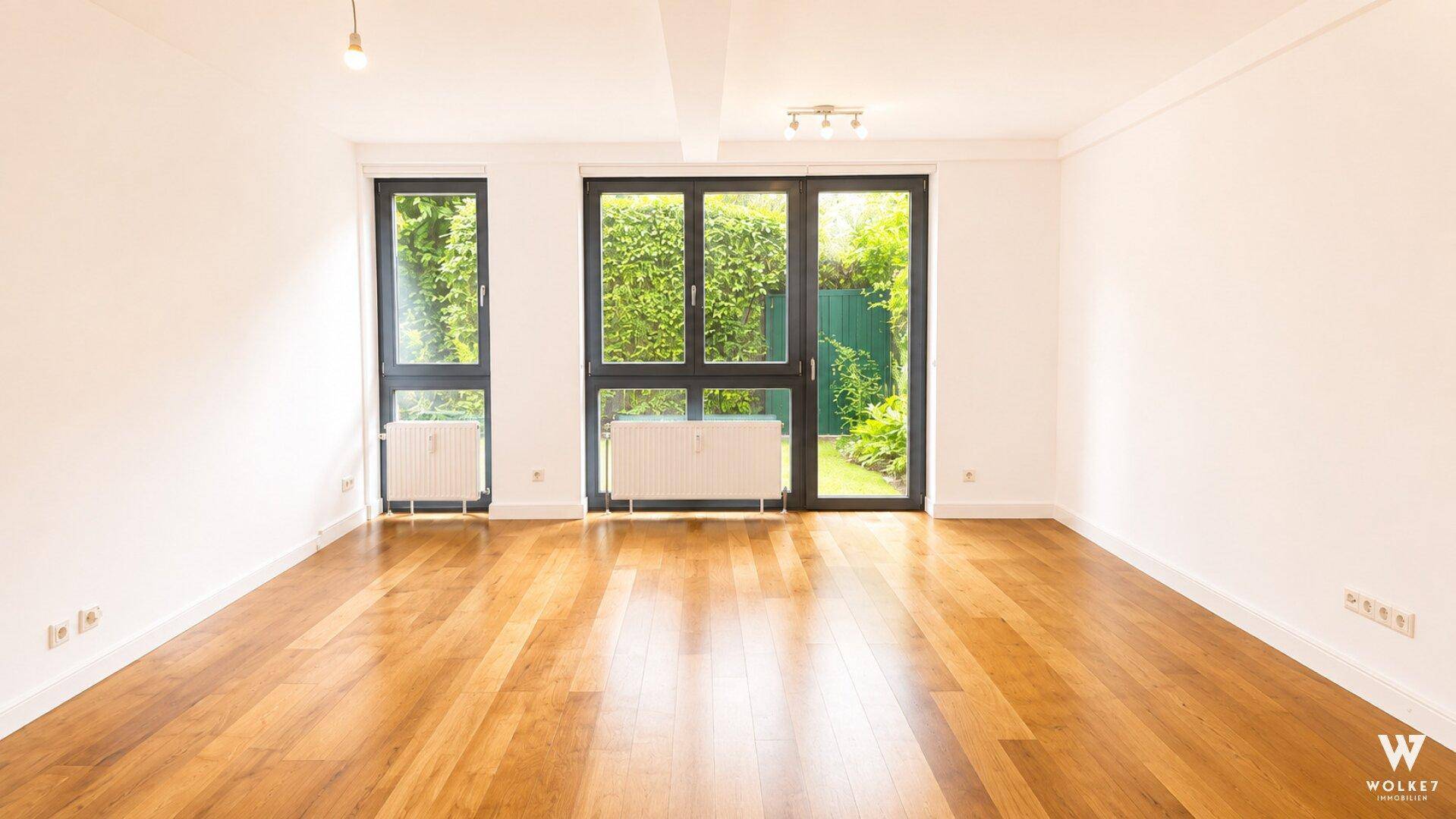 Heller Wohnraum mit Holzboden, großen Fenstern und direktem Zugang zum grünen Garten.