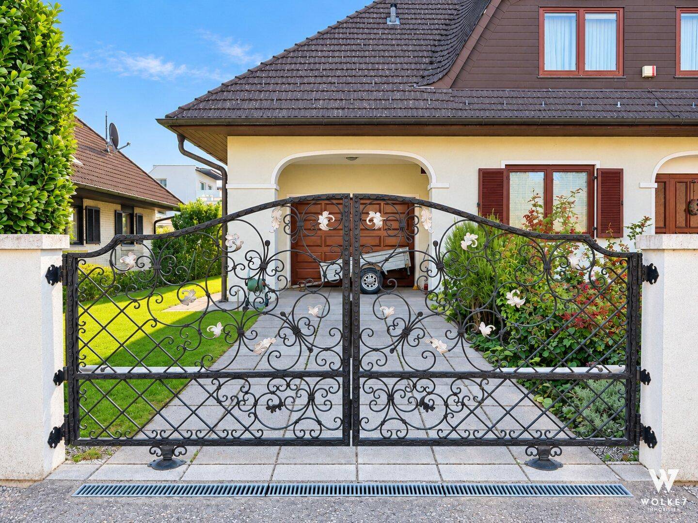 Dekoratives schmiedeeisernes Tor am Eingang zur gepflasterten Einfahrt des Hauses.