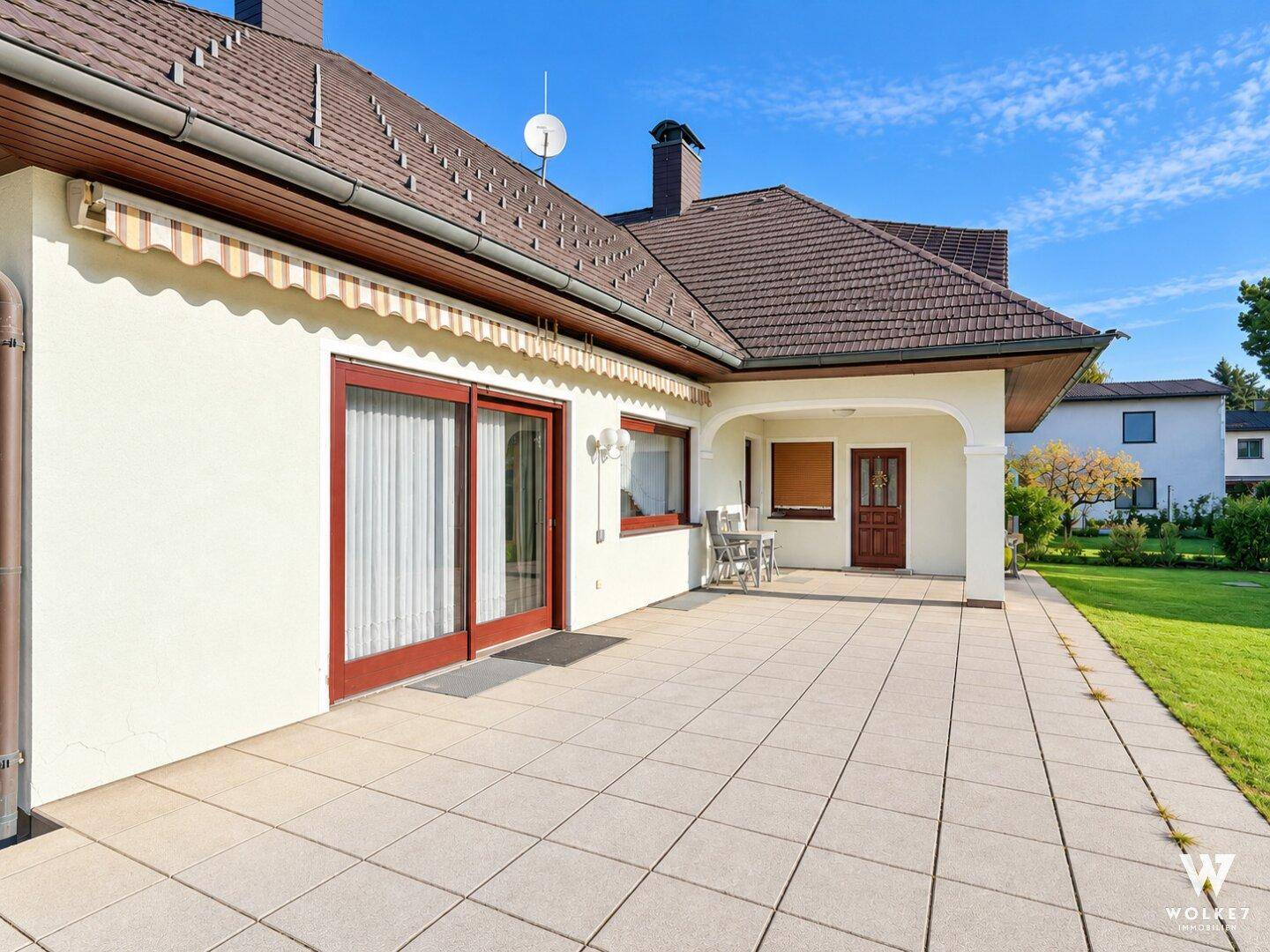 Geräumige, geflieste Terrasse an der Hausseite mit Markise und Zugang zum Garten.