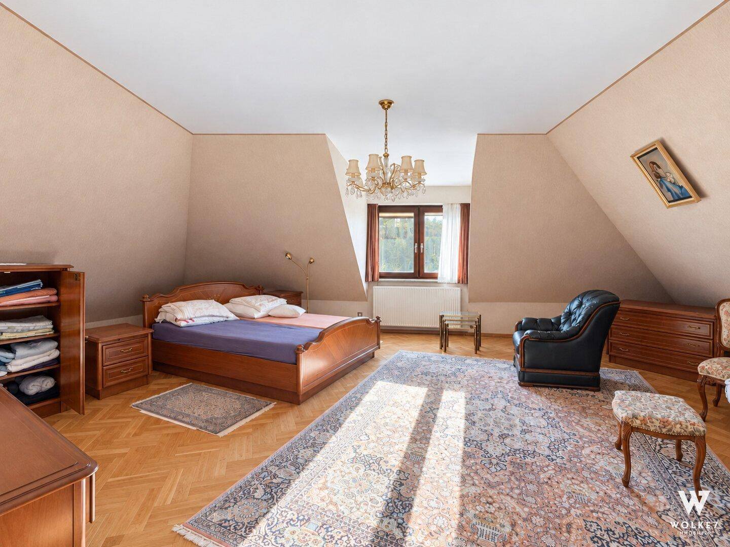 Geräumiges Schlafzimmer im Dachgeschoss mit schrägen Wänden, Parkettboden und großem Bett.