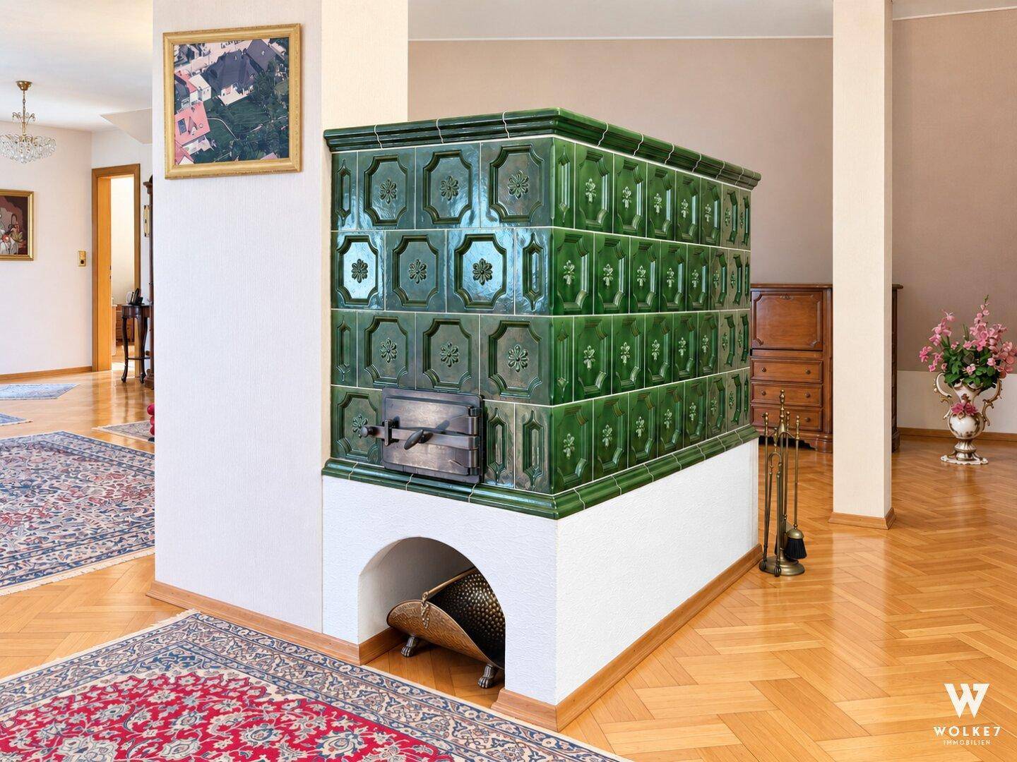 Detailansicht eines traditionellen grünen Kachelofens mit dekorativen Fliesen und Holzlegefach.
