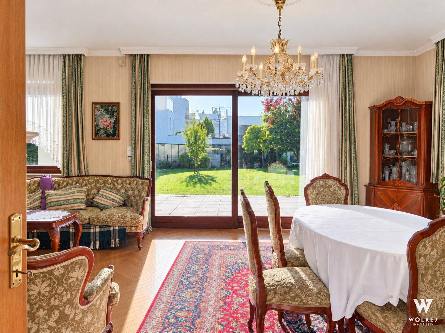 Klassischer Wohn-Essbereich mit elegantem Kronleuchter, Parkettboden und Zugang zur Terrasse mit Gartenblick.