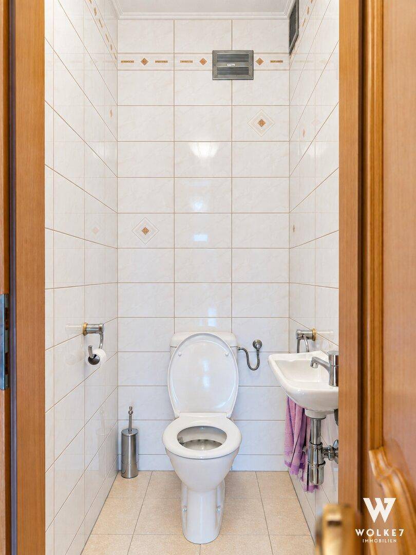Kleines Gäste-WC mit Toilette, Waschbecken und hellen Fliesen.