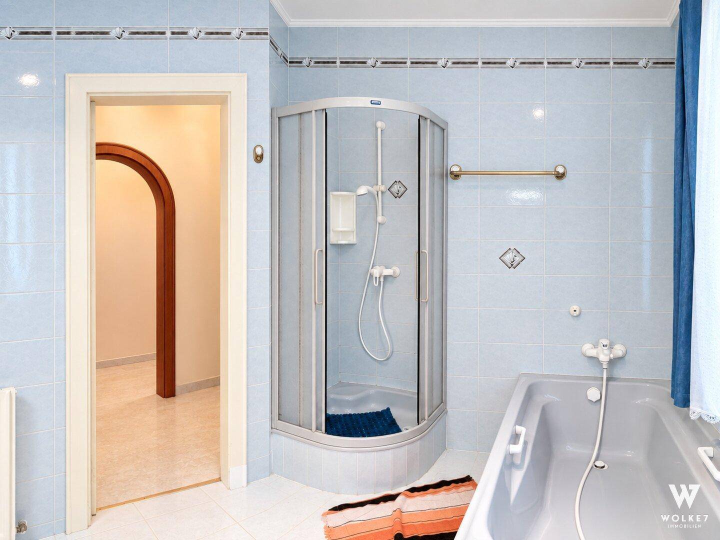 Badezimmer mit Duschkabine, Badewanne und hellblauen Fliesen.