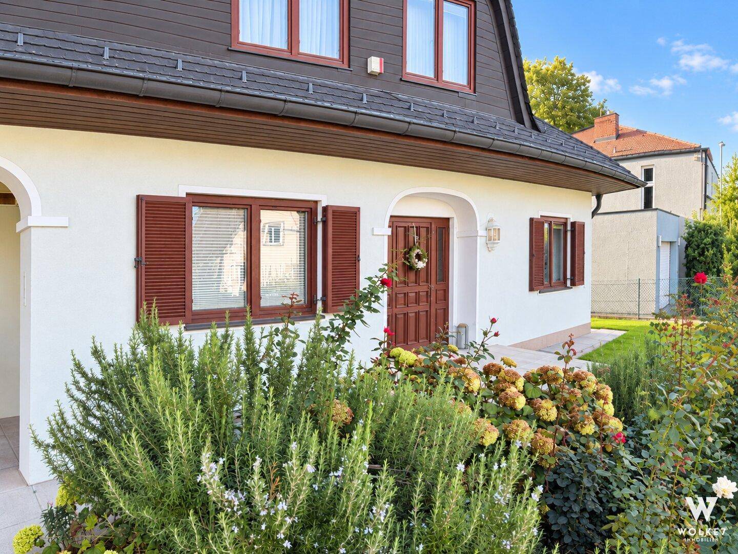 Detailansicht des Hauseingangs mit Blumenbeeten und traditionellen Fensterläden.