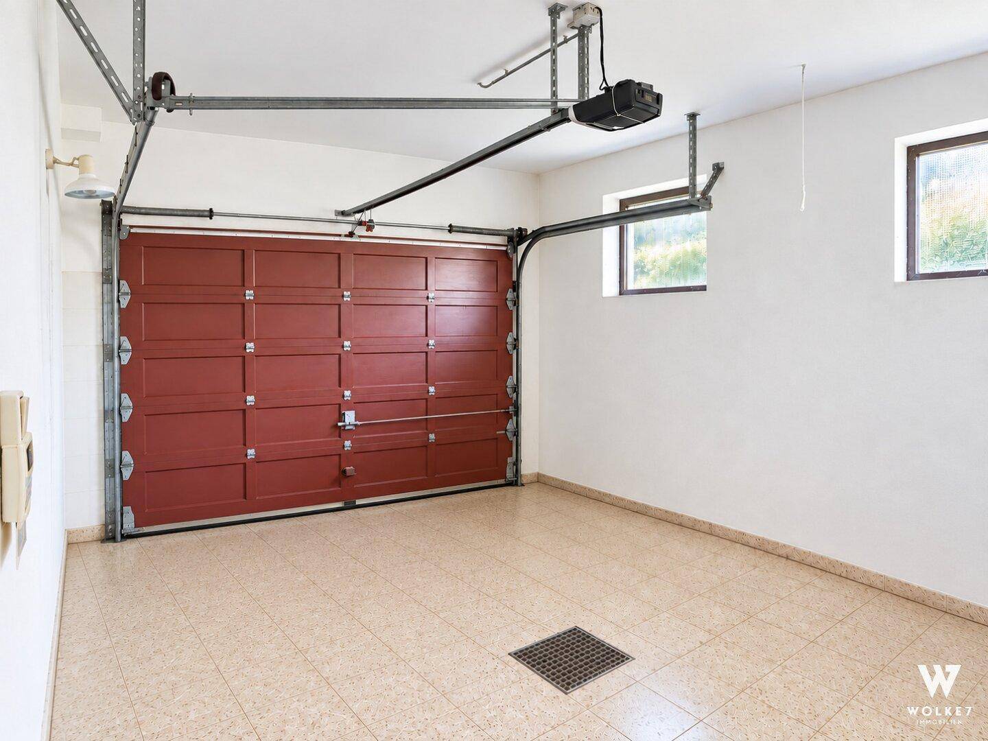 Geräumige Garage mit rotem Tor, Fliesenboden und zwei Fenstern.