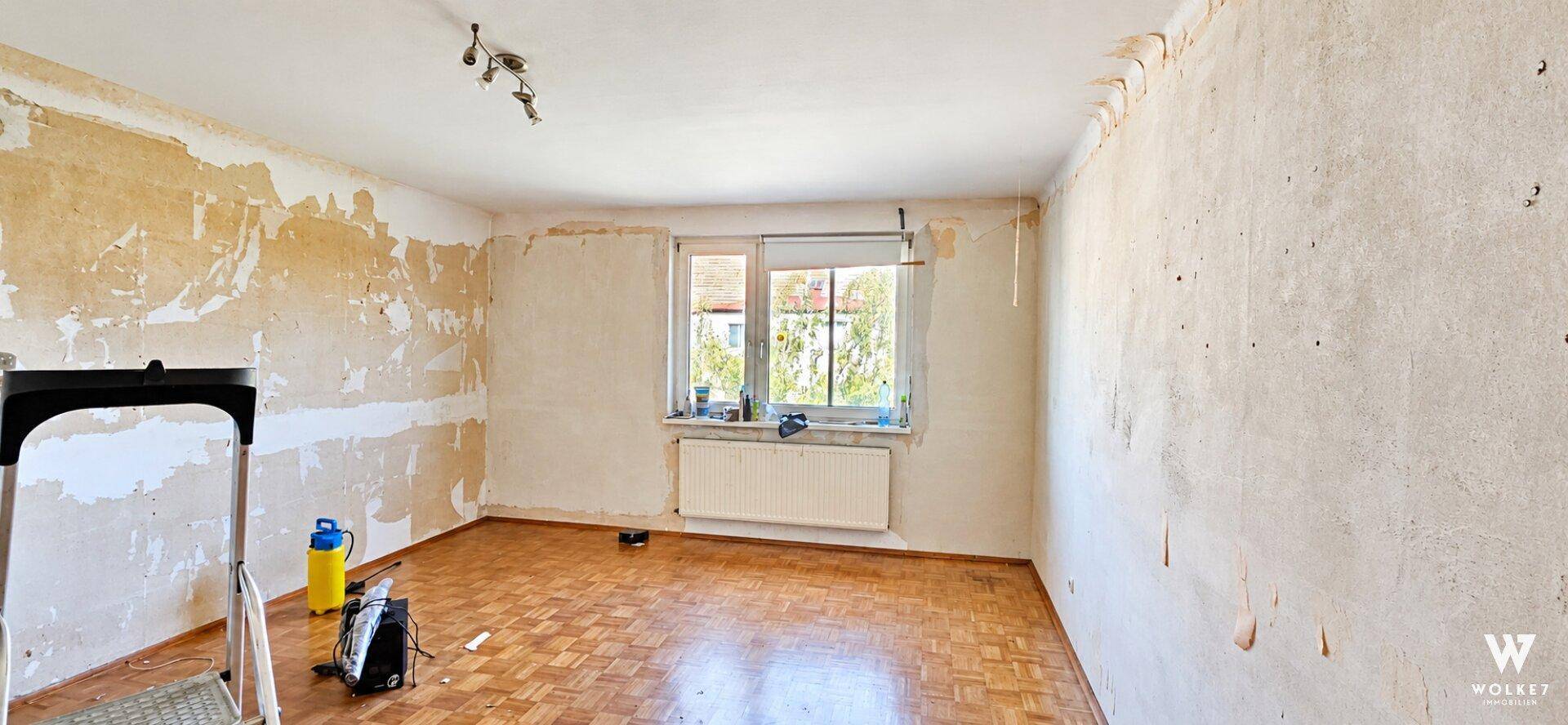 Leerer Raum in Renovierung mit teilweise entfernter Tapete und Parkettboden.