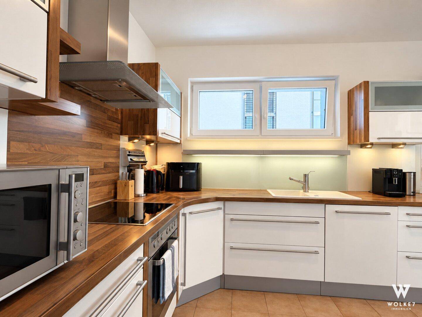 Moderne Einbauküche mit Holzarbeitsplatten, weißen Fronten und Fenster.