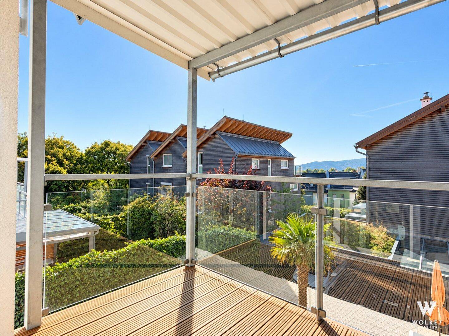 Geräumiger Balkon mit Holzboden, Glasgeländer und weitem Blick ins Grüne.
