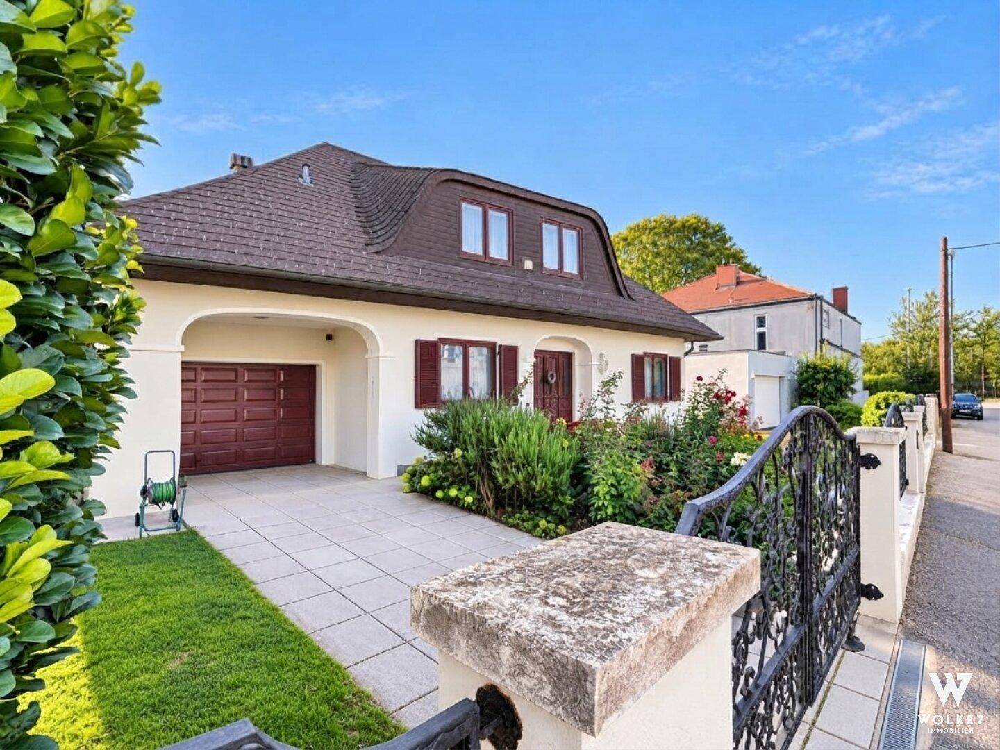 Vorderansicht des Hauses mit gepflasterter Einfahrt, Garage und gepflegter Bepflanzung.