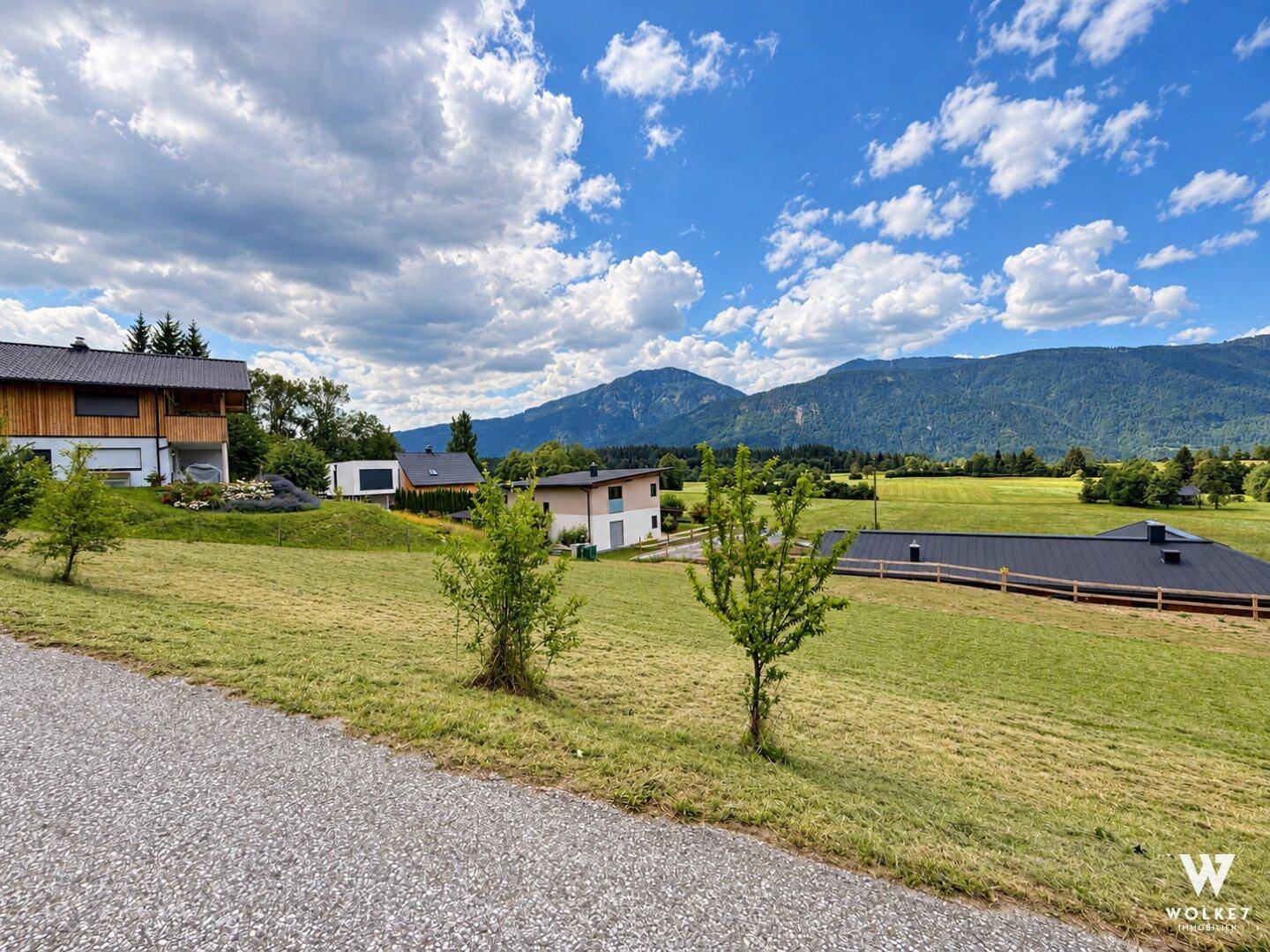Weitläufige Landschaft mit grünen Wiesen, vereinzelten Häusern und majestätischem Bergblick.