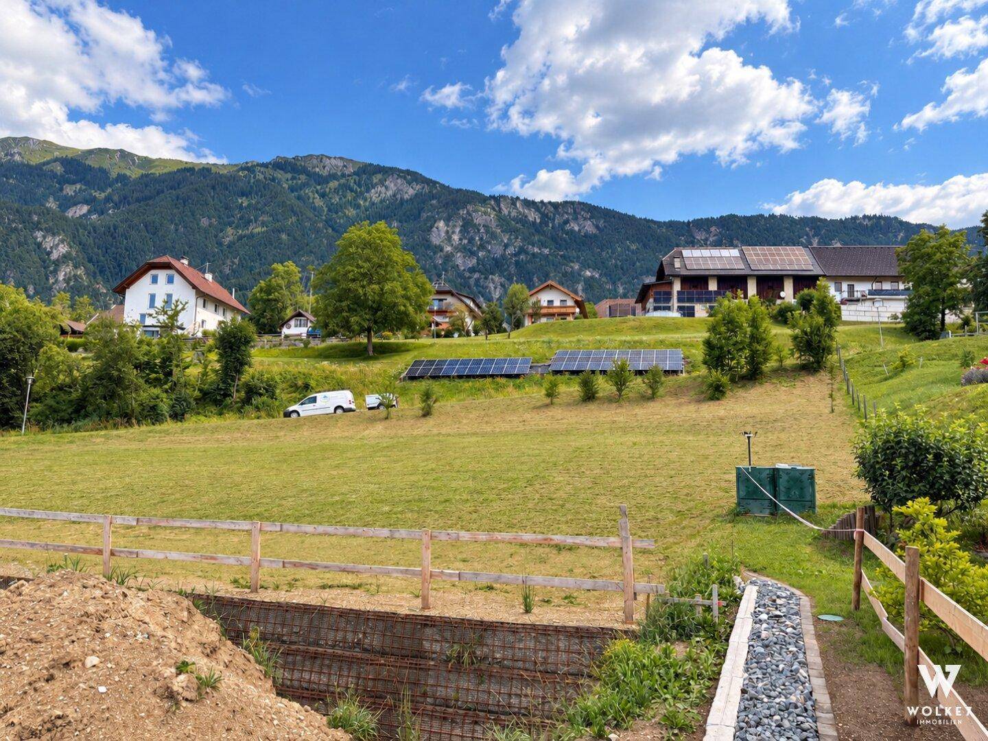 Grundstück mit Solaranlagen im Hintergrund, umgeben von grünen Wiesen und Bergen.