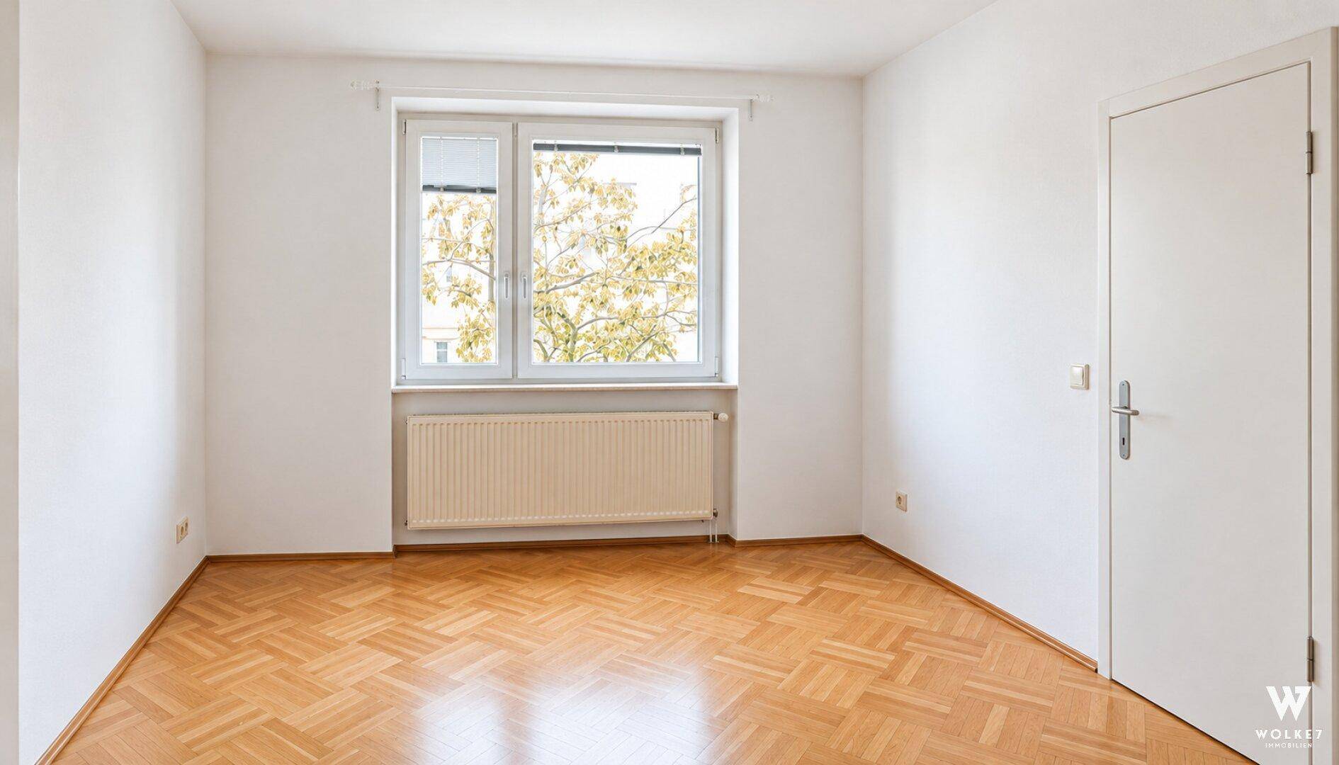 Unmöblierter Raum mit Fischgrätparkett, weißen Wänden und einer weißen Tür.