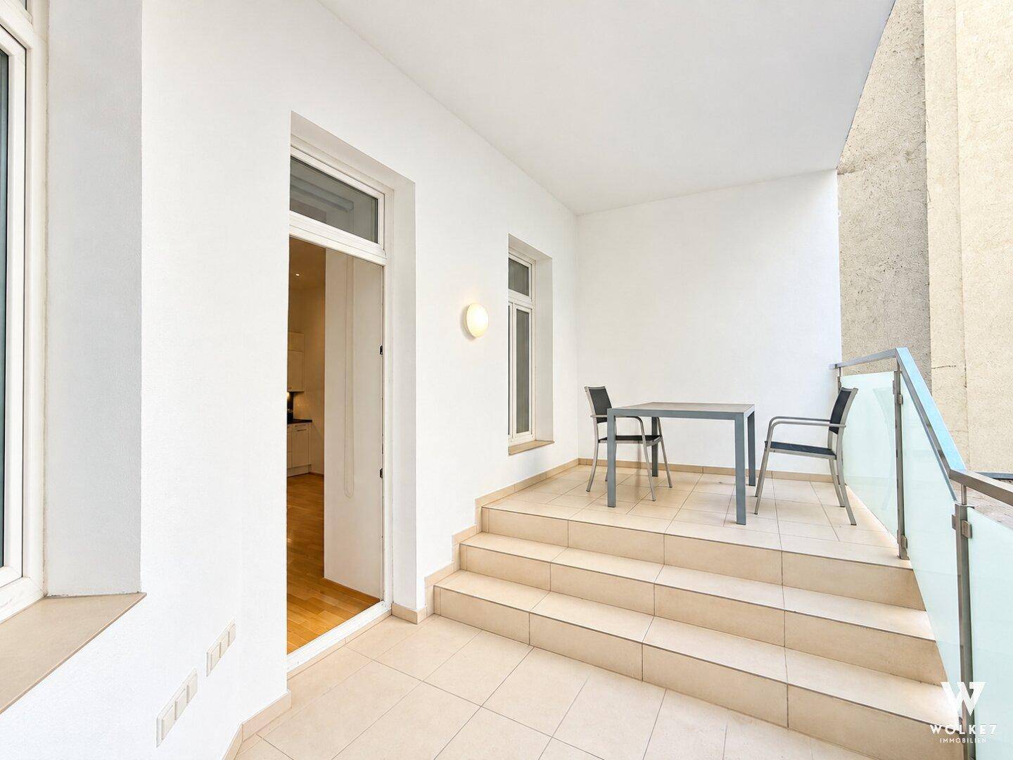 Heller Balkon mit Fliesenboden, Sitzgelegenheiten und Blick auf die Umgebung.