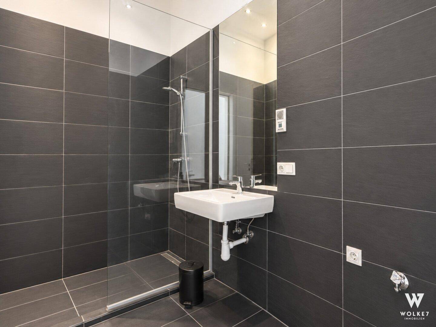 Modernes Badezimmer mit großer begehbarer Dusche und dunklen Fliesen.