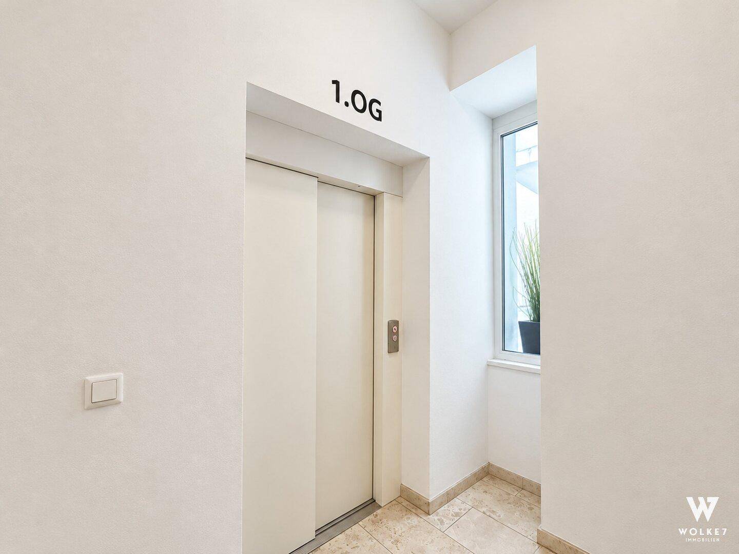 Heller Flur mit Aufzug und Fenster, der Zugang zu den Wohnungen bietet.