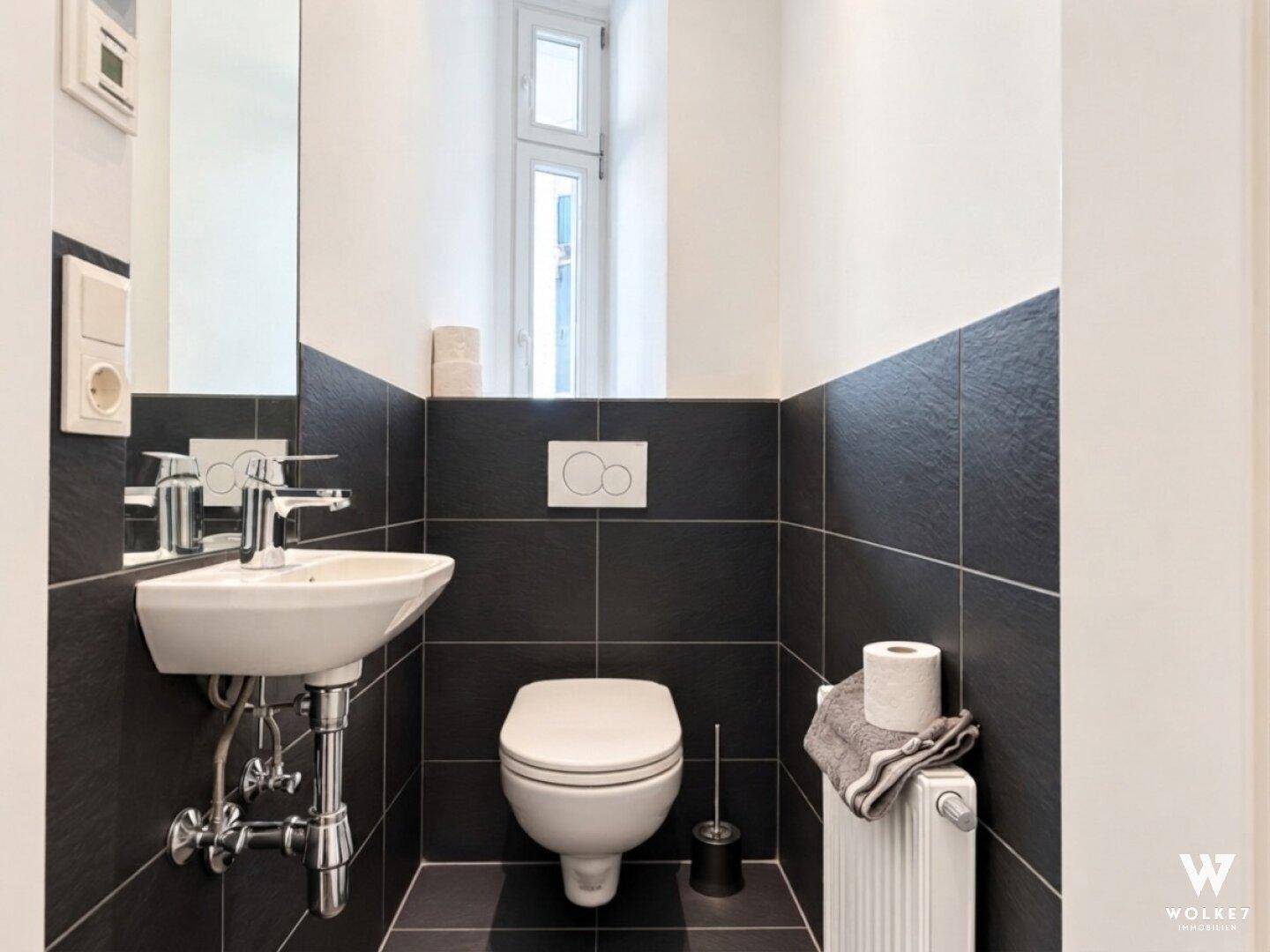 Modernes Gäste-WC mit Wand-WC, Waschbecken und dunklen Wandfliesen.