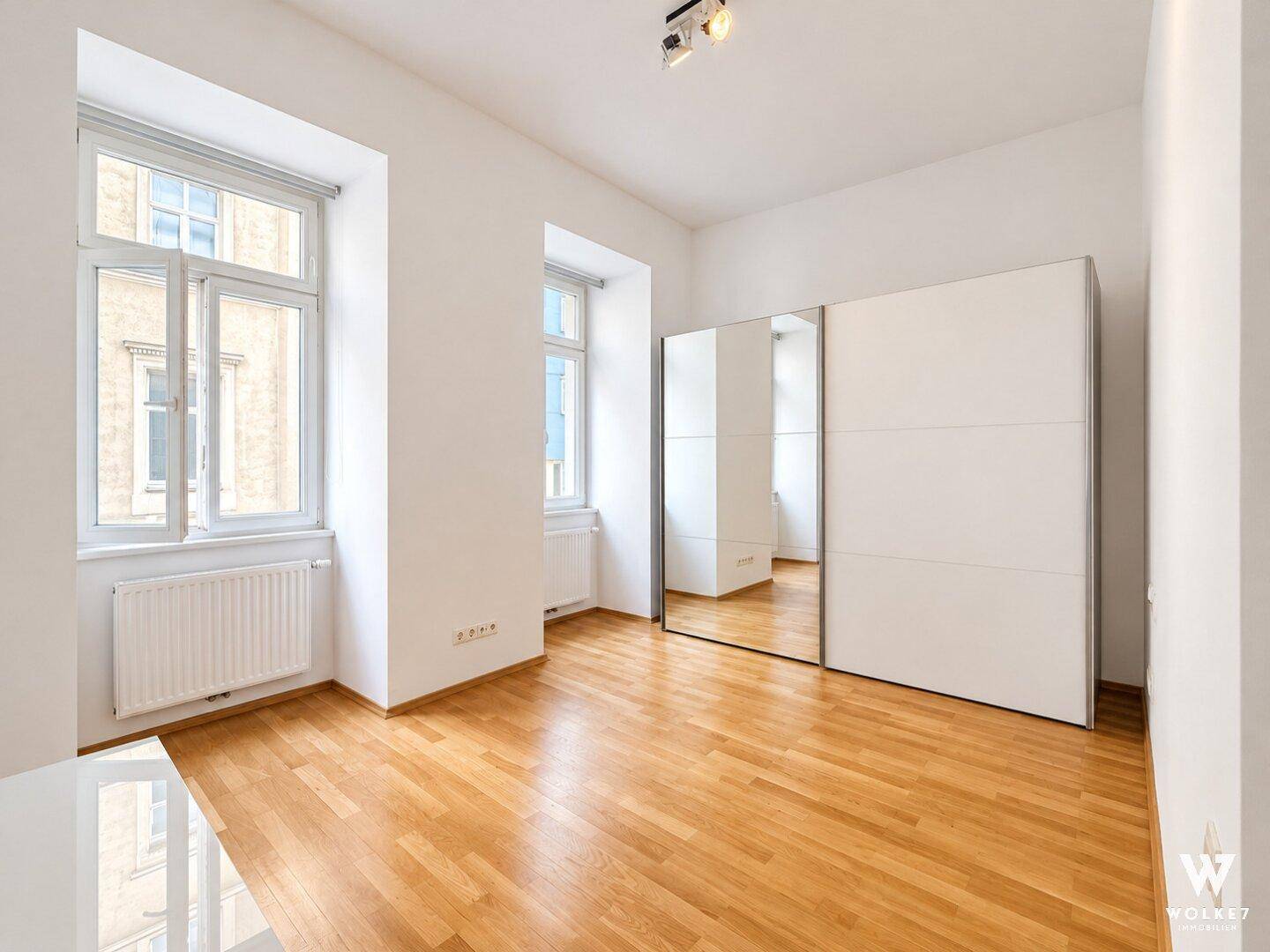 Helles Schlafzimmer mit Holzboden und großem Spiegelschrank.