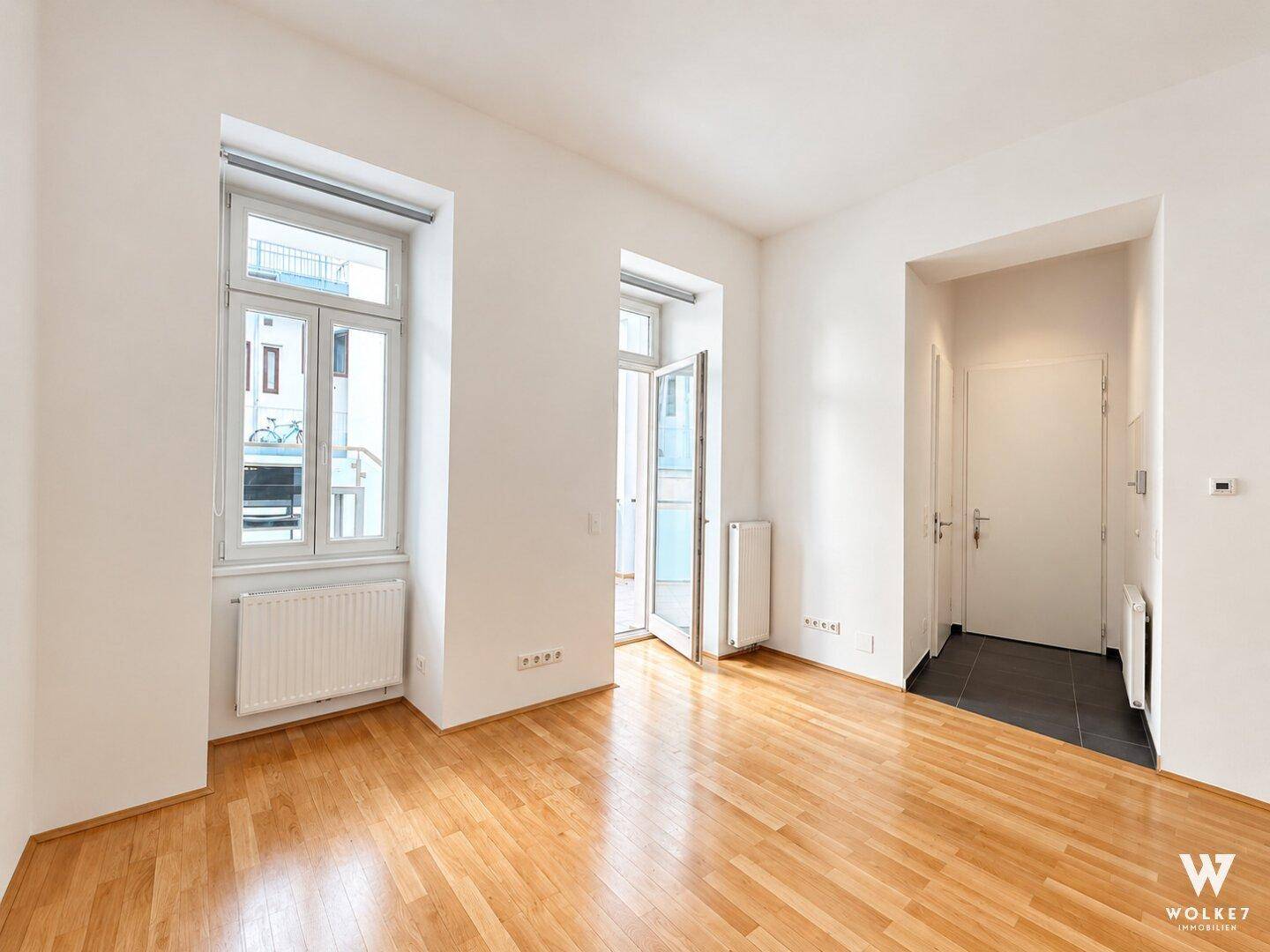 Geräumiges, helles Wohnzimmer mit Holzboden und Zugang zu einem kleinen Balkon.