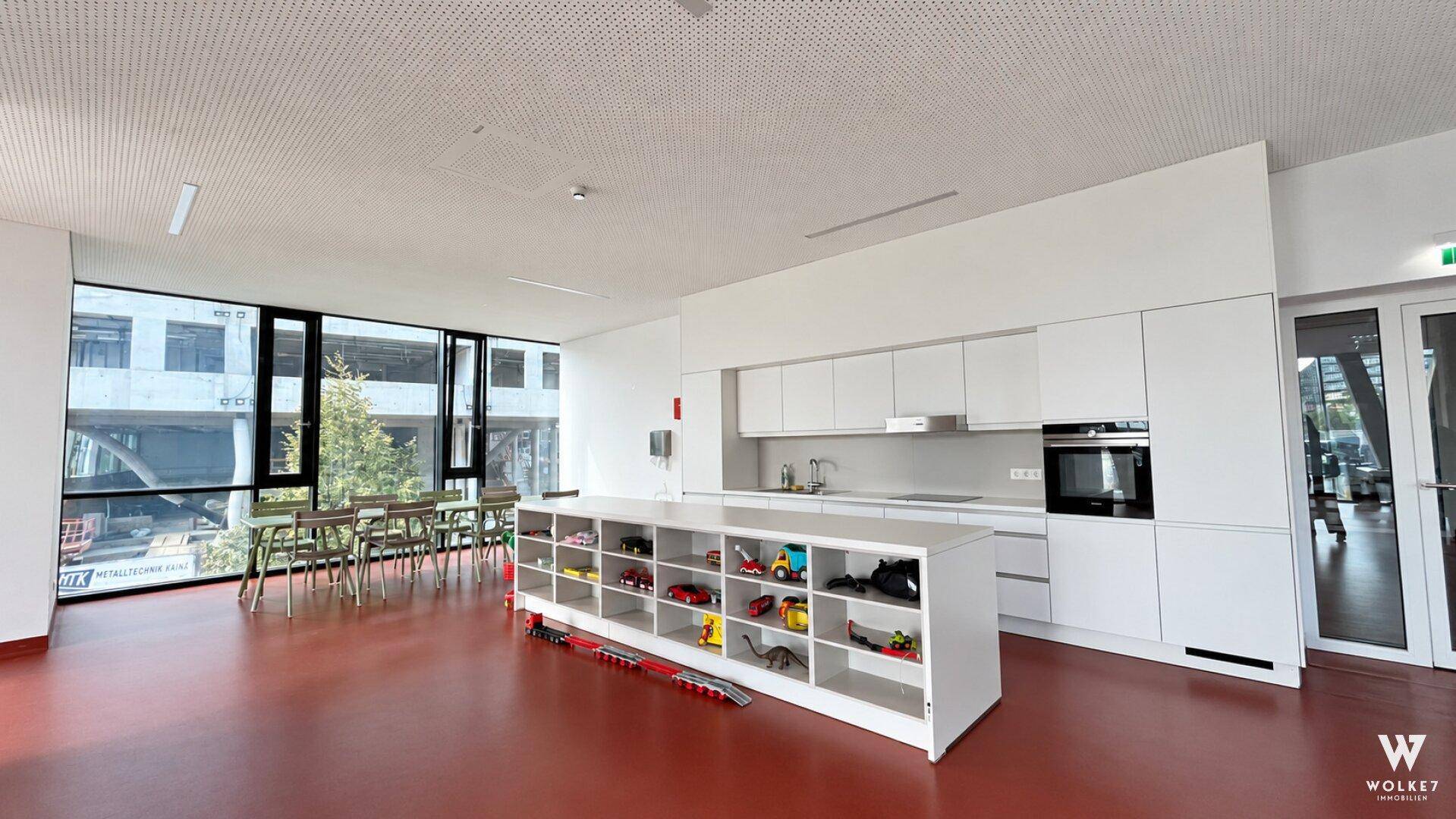 Heller Gemeinschaftsraum mit Küche, Essbereich und Spielzeugregal für Kinder.