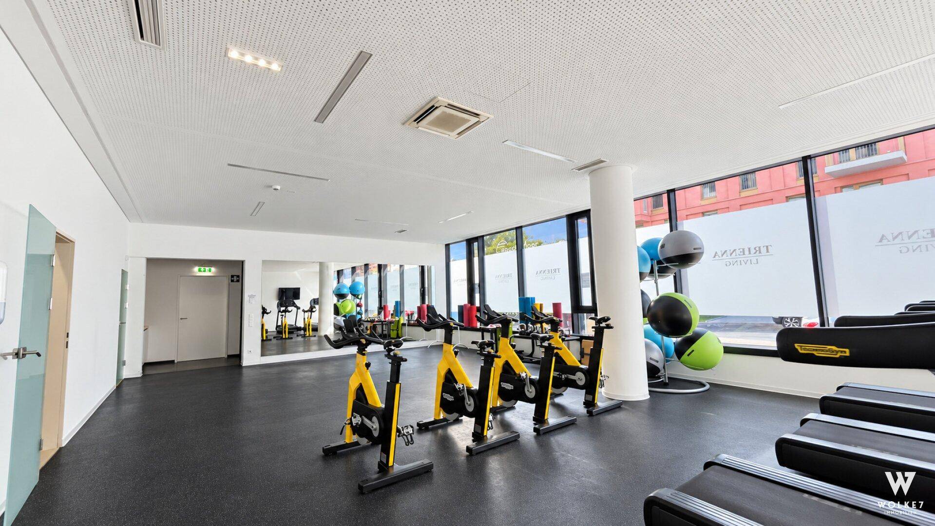 Moderner Fitnessraum mit verschiedenen Trainingsgeräten und großen Fenstern.
