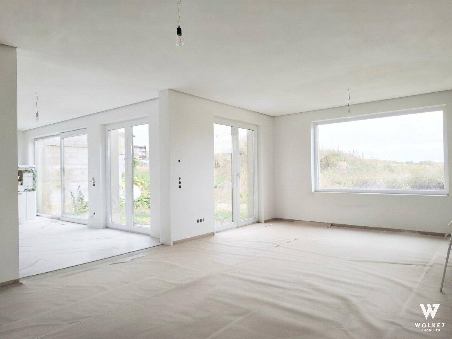 Großer, heller Raum im Neubau mit vielen Fenstern und Zugang zum Außenbereich.