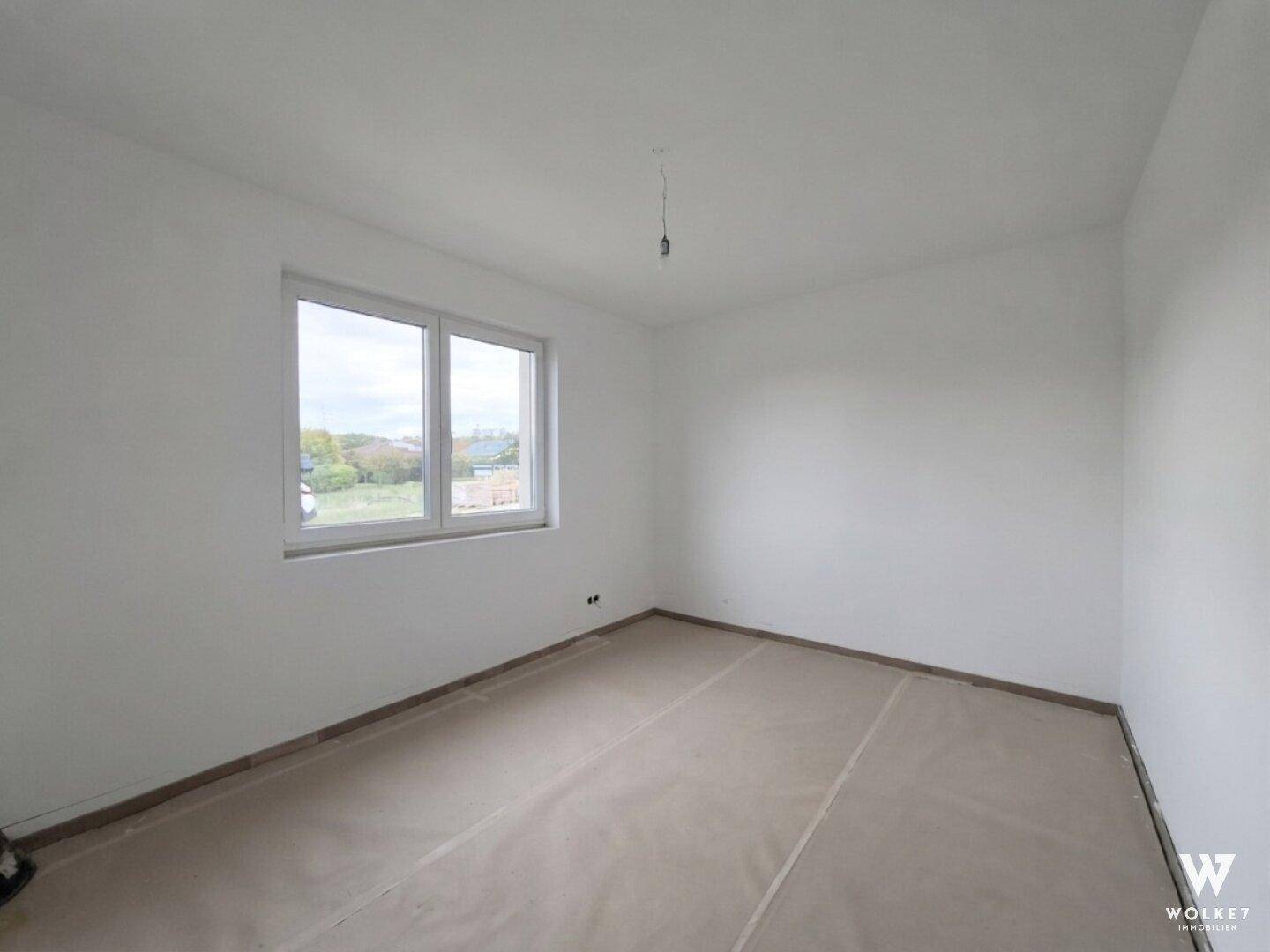 Helles Schlafzimmer im Neubau mit großem Fenster und Blick ins Grüne.