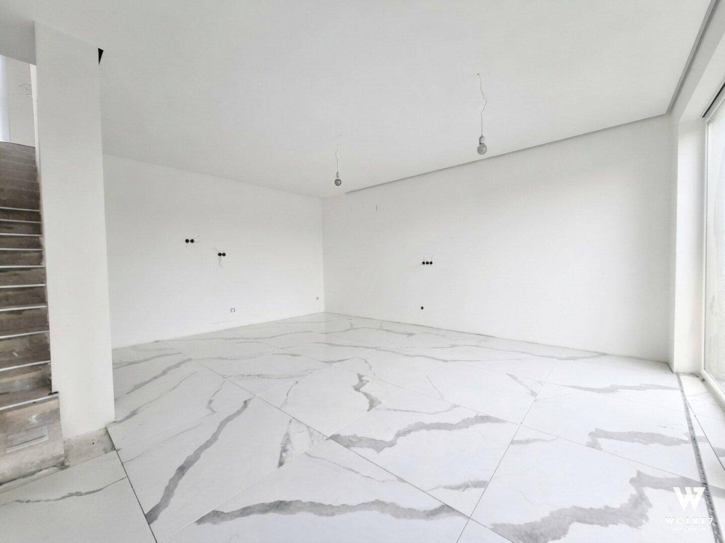 Geräumiger, heller Wohnbereich im Neubau mit moderner Treppe und Fliesenboden.